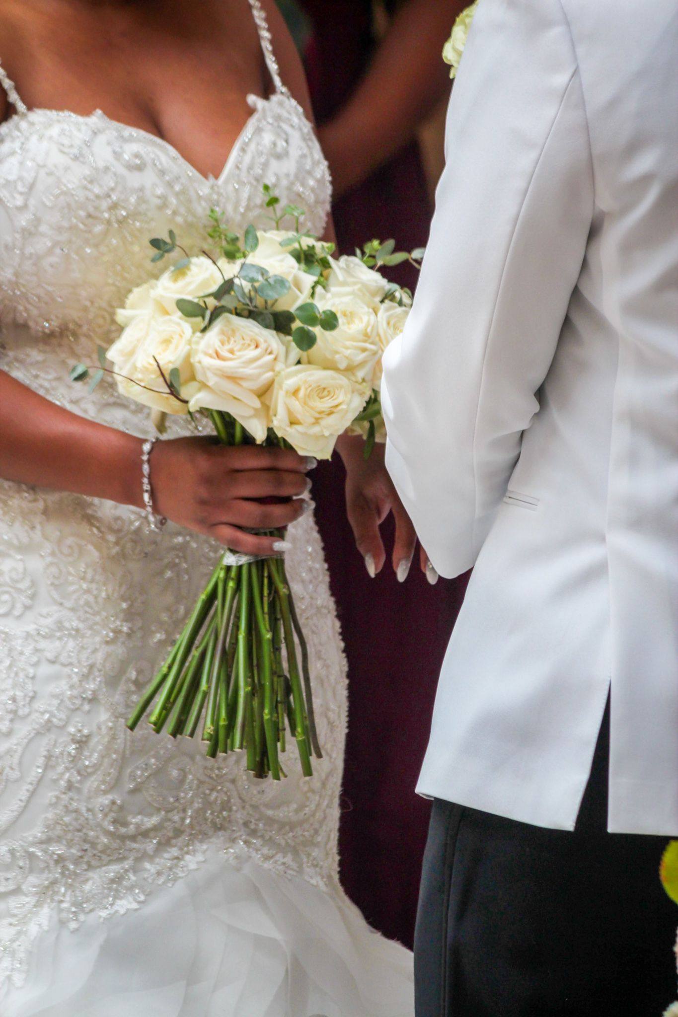Close-up details of white rose wedding bouquets held against formal attire.