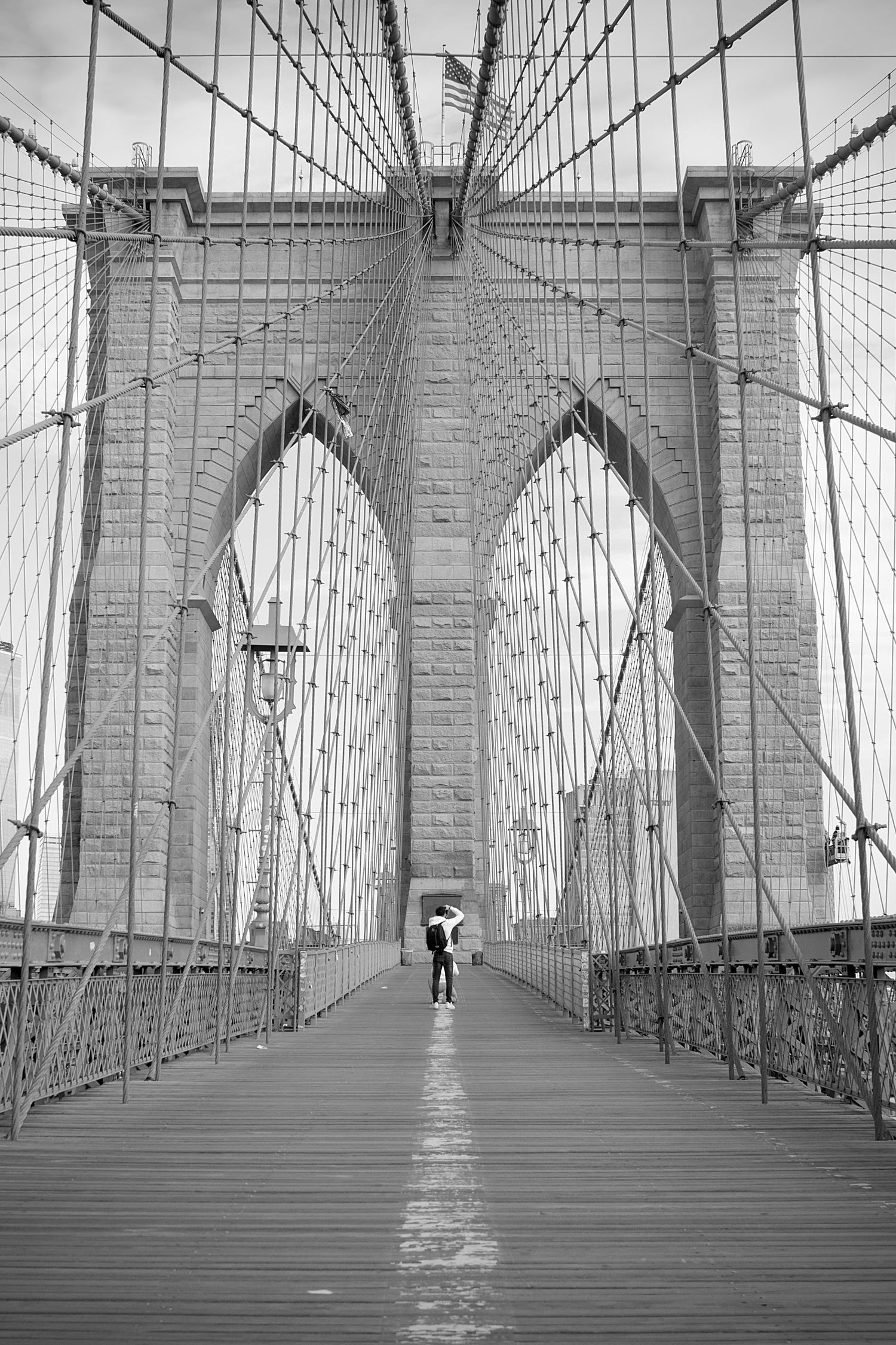Black and white photograph of Brooklyn Bridge walkway with dramatic vanishing point perspective.