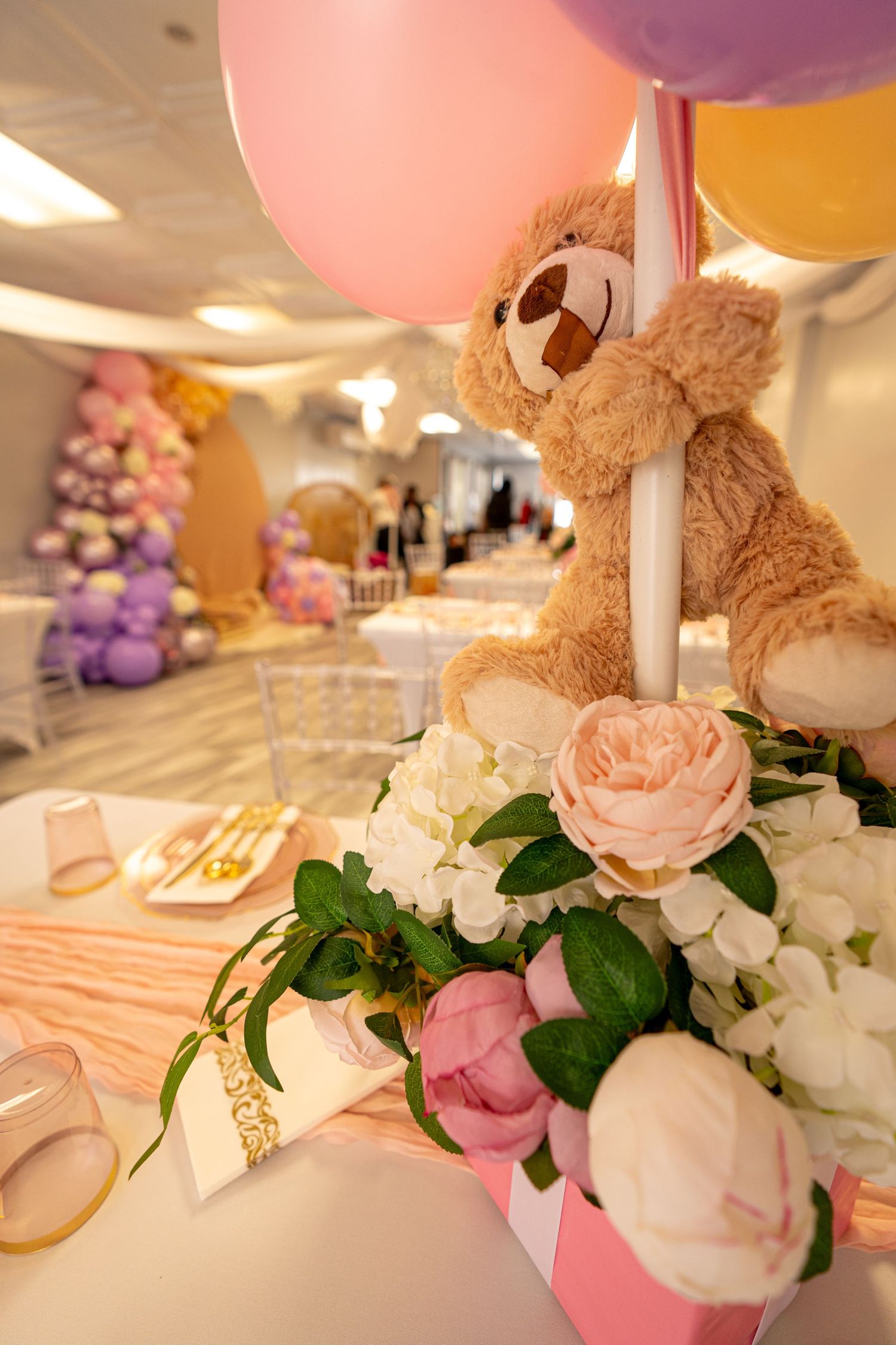 Baby shower decorations with pink balloons, teddy bears, and floral arrangements.