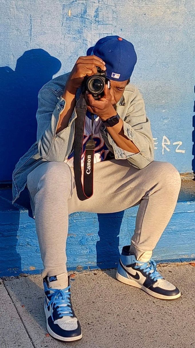 Photographer in casual wear crouches low while taking photos with a camera against a blue background.