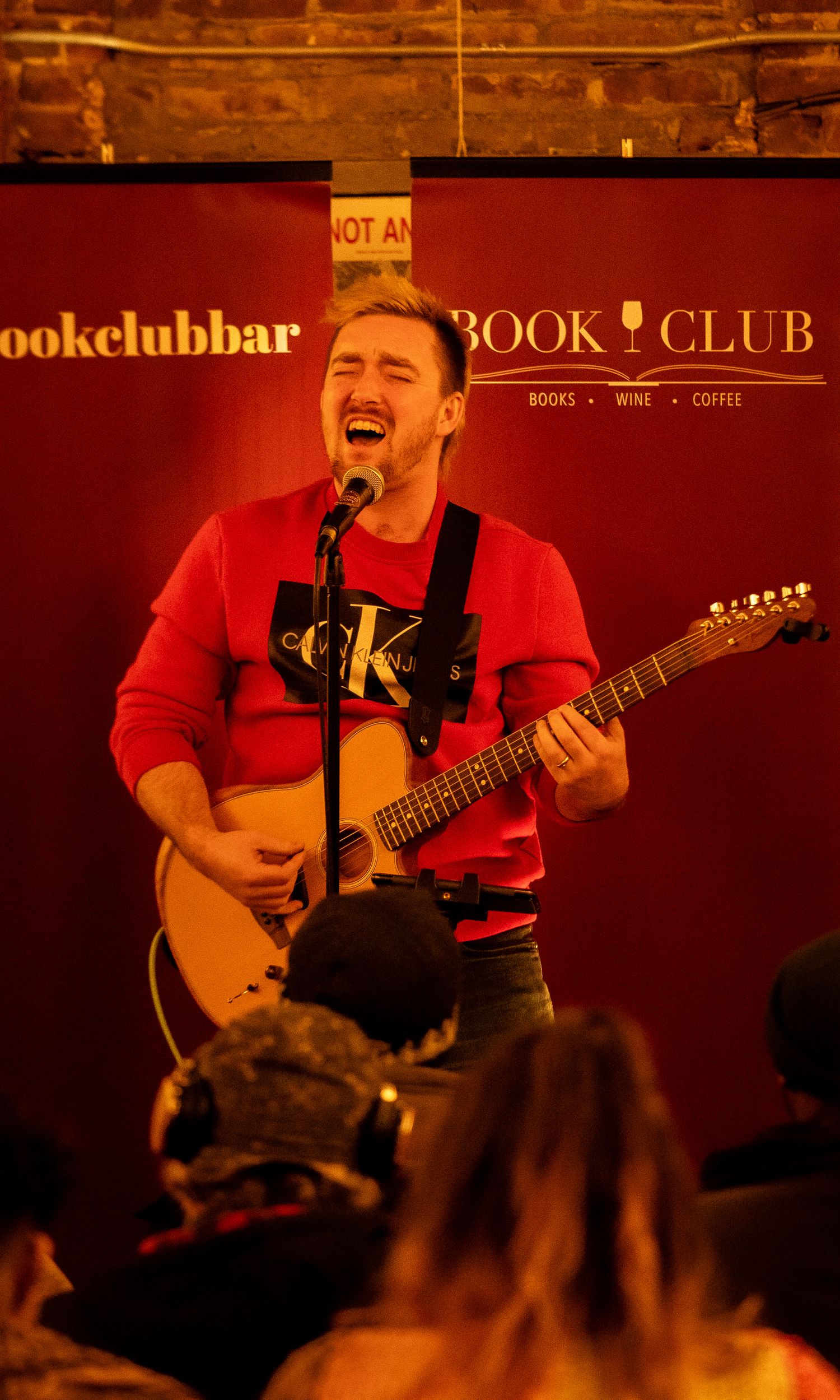 Musician playing guitar and singing at Book Club Bar with warm lighting.