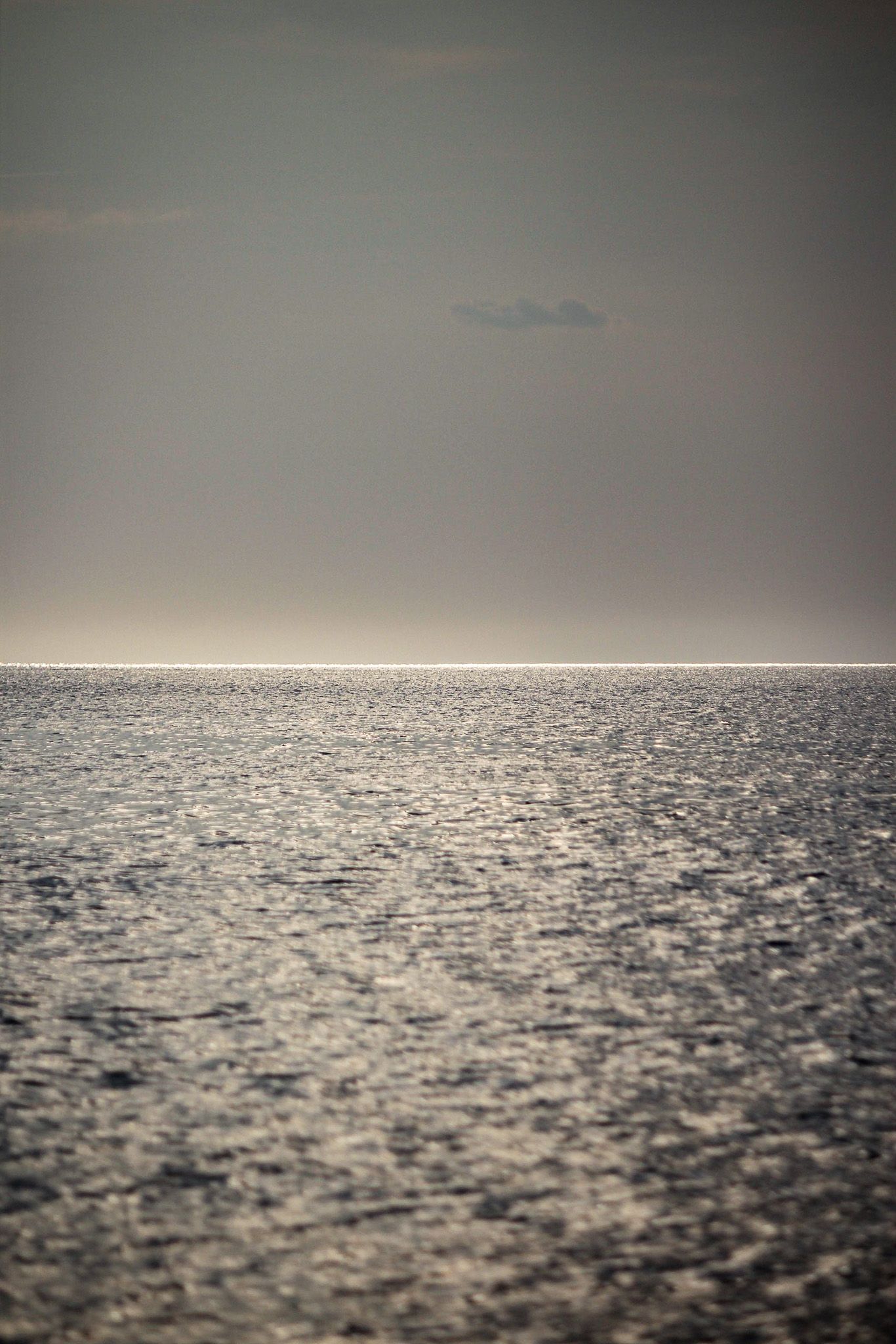 Minimalist seascape with silver water reflecting light under moody gray sky.