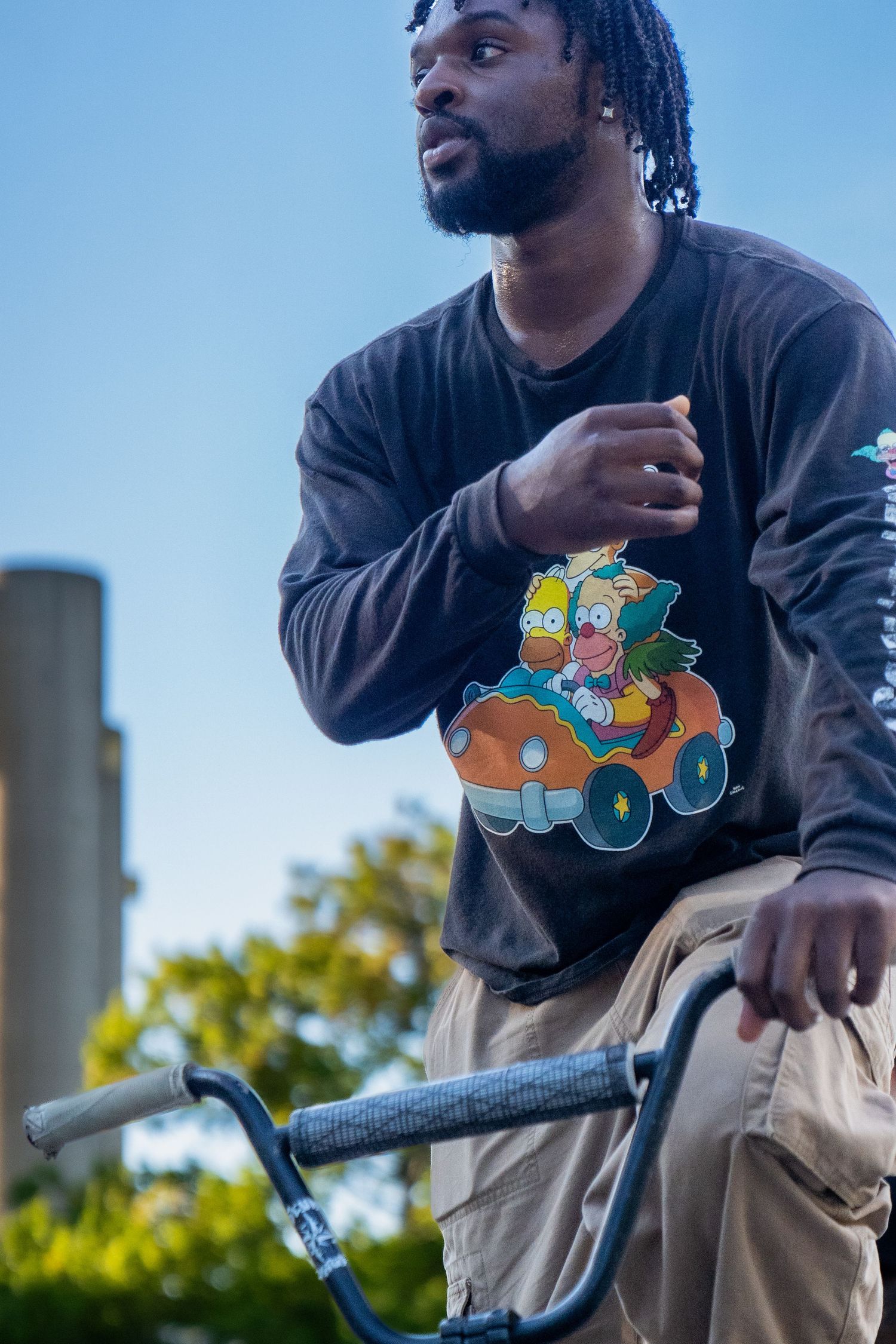 BMX cyclist wearing cartoon graphic sweatshirt leans on handlebars outdoors.