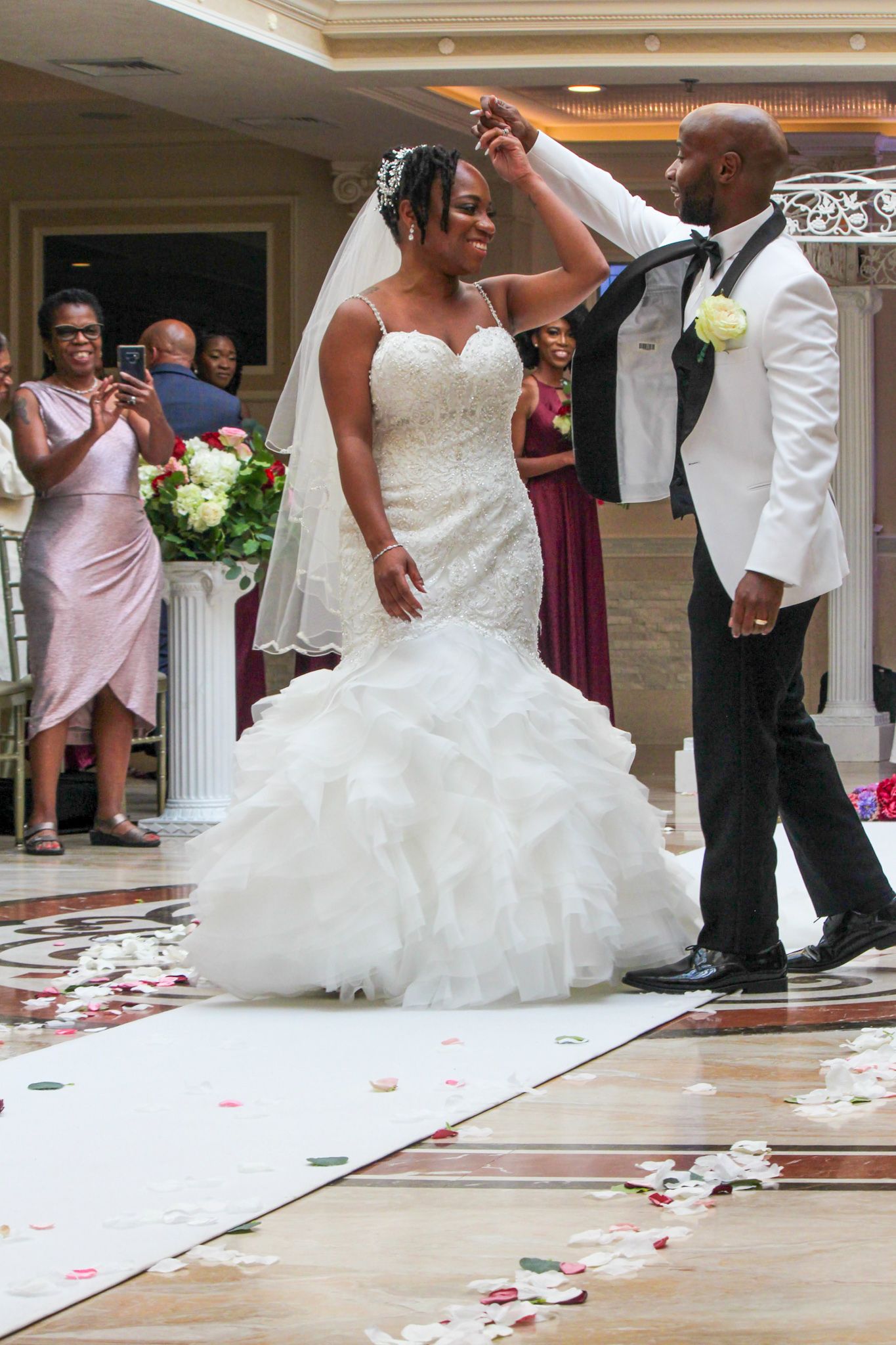 Wedding couple dancing on a white aisle runner decorated with rose petals in an elegant venue.