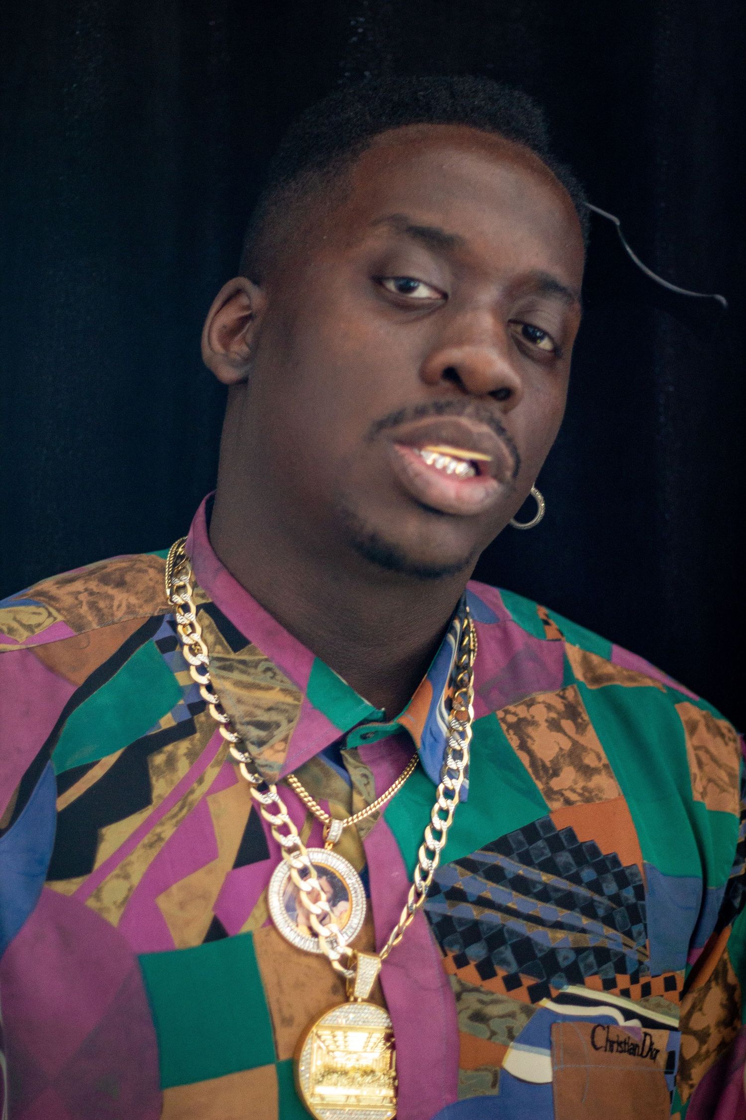 Person wearing colorful patterned shirt with gold chain necklace against dark background.