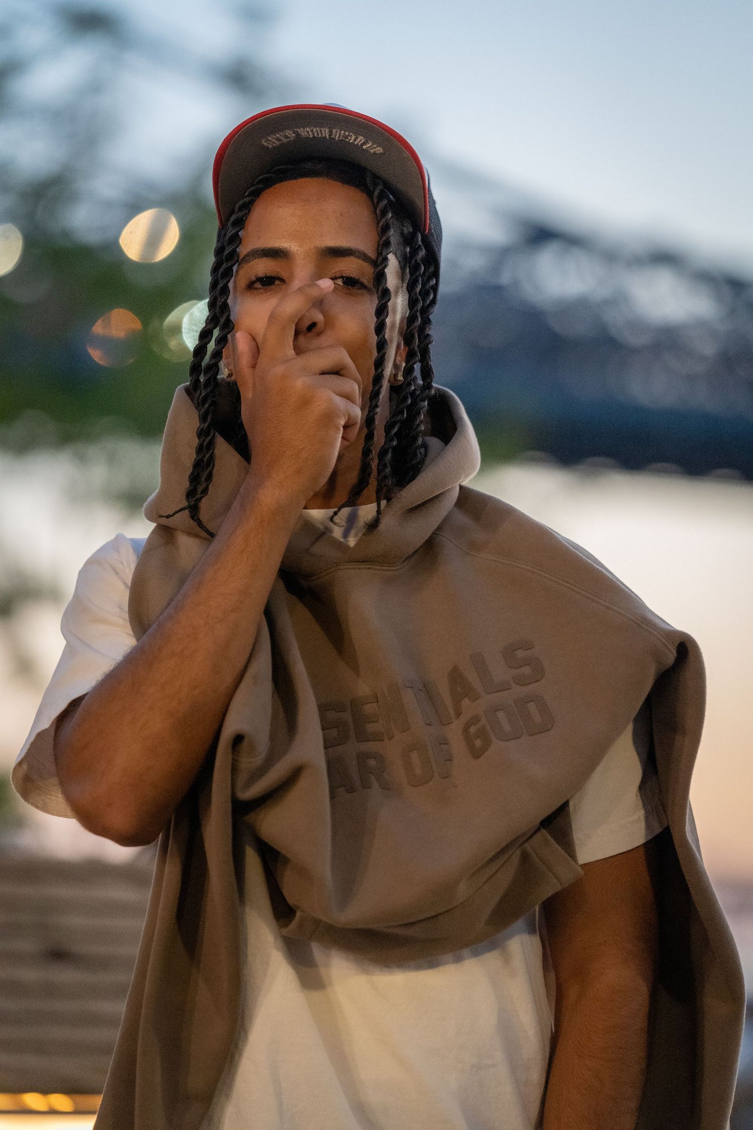 A person in casual clothing gestures while standing outdoors.