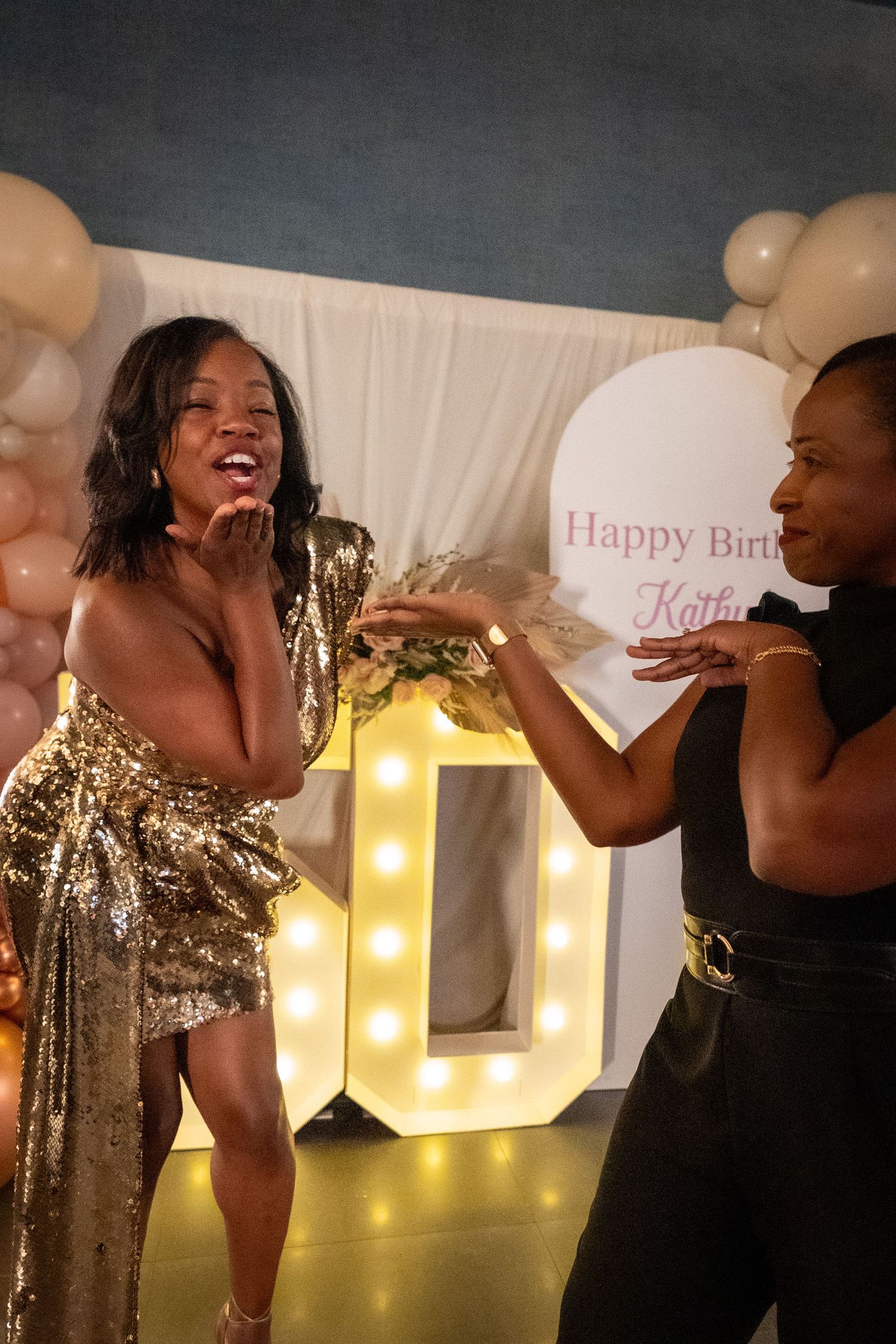 Birthday celebration with illuminated letters and guests in gold and black attire.