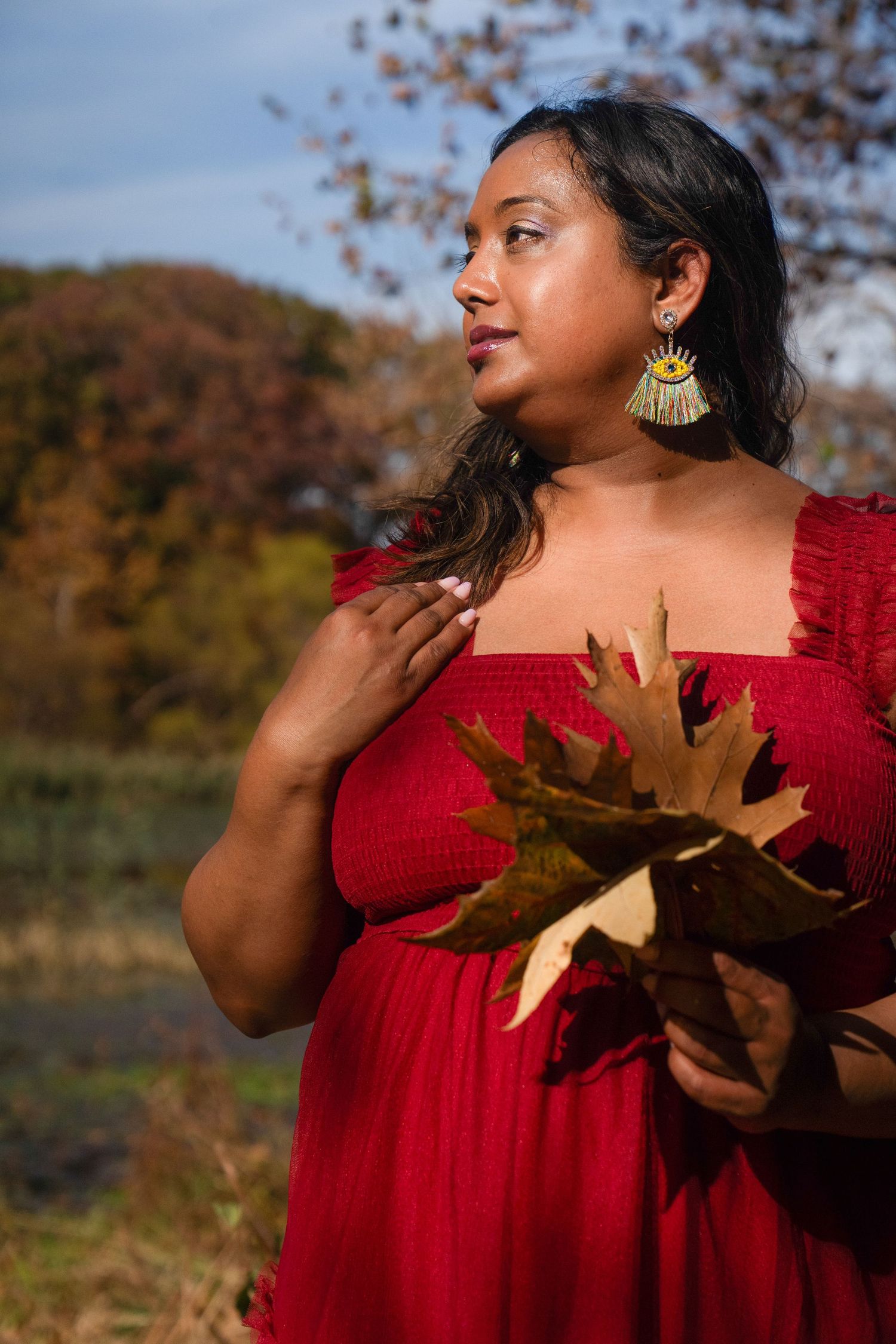 Woman in red dress holding autumn leaves during outdoor photoshoot.