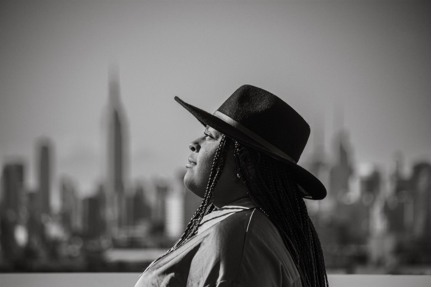 Silhouette of person wearing hat against city skyline in black and white.