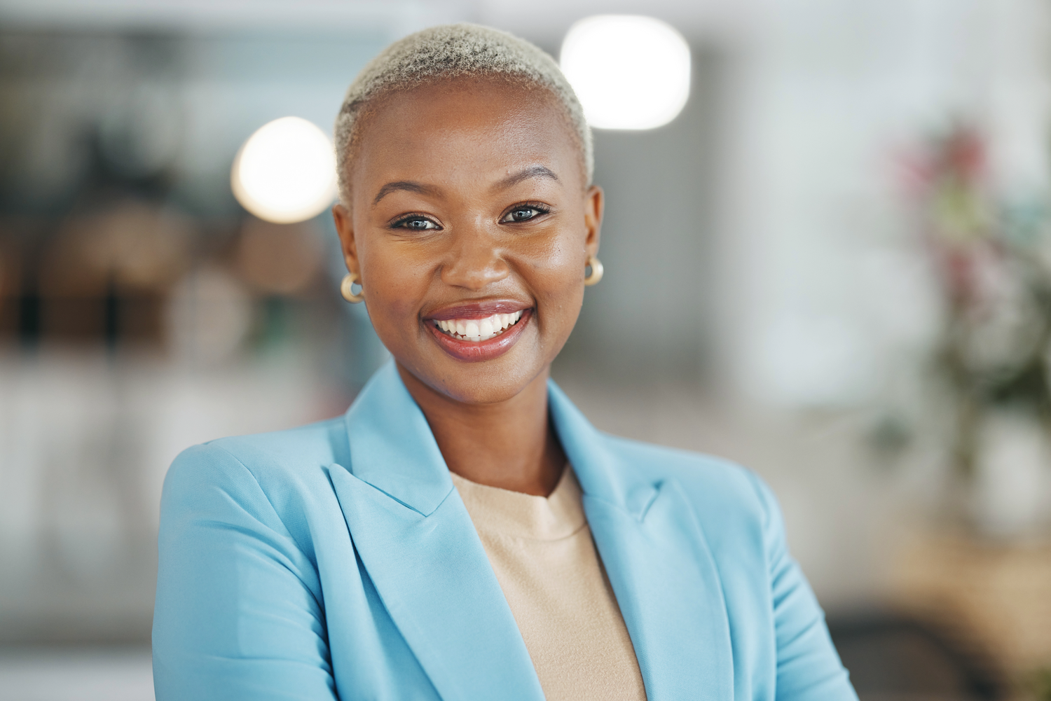 Professional in a light blue blazer and beige top smiles warmly in an office setting.