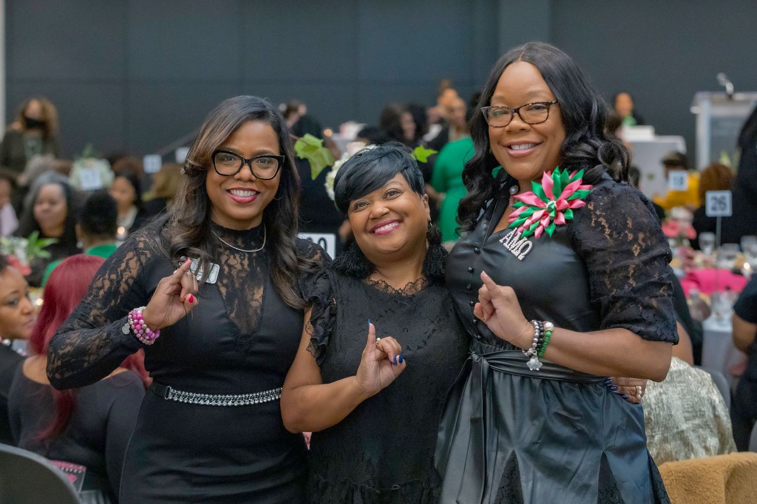 Three attendees pose together at a formal event wearing elegant black attire.
