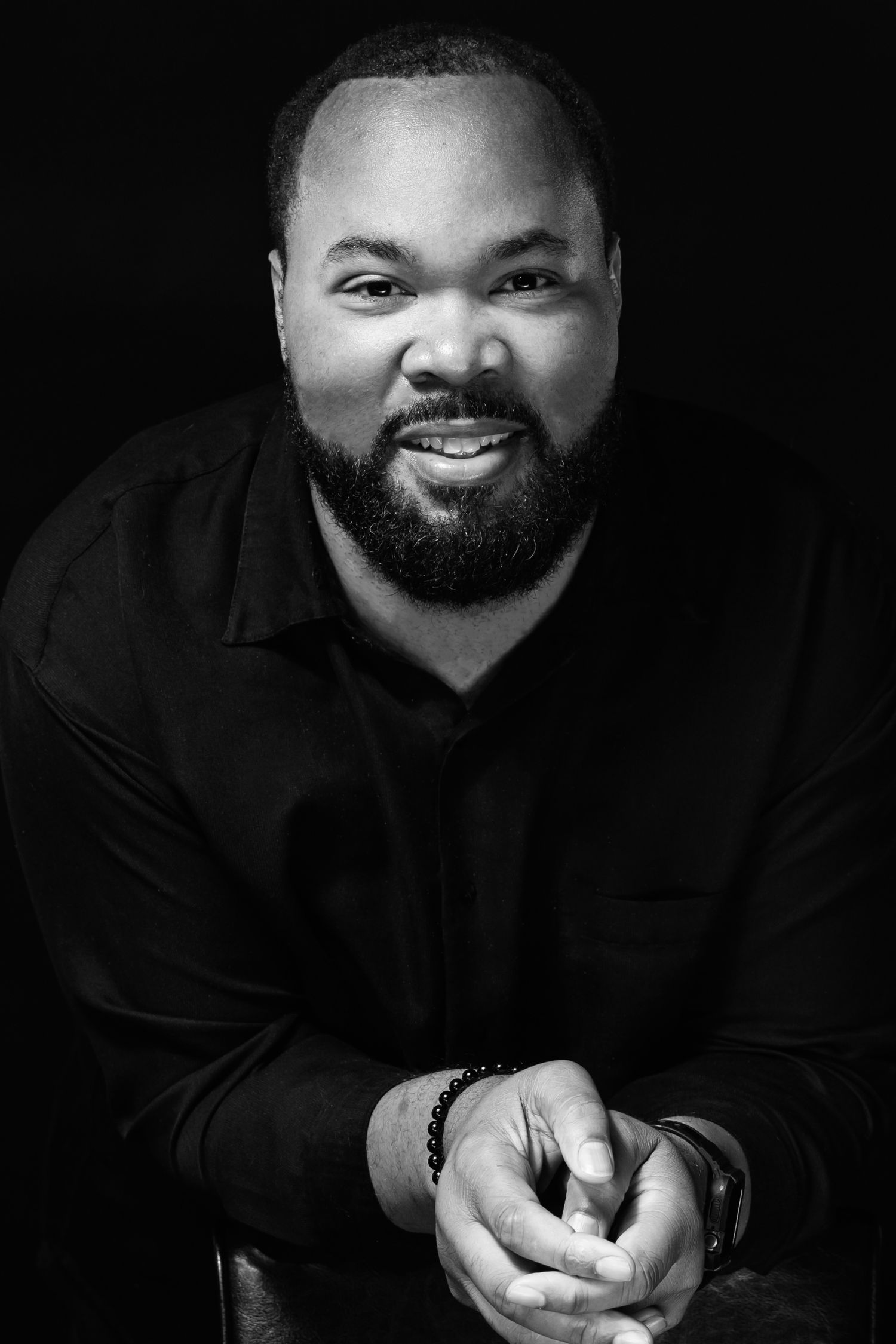 Black and white portrait of man in dark shirt with warm expression.