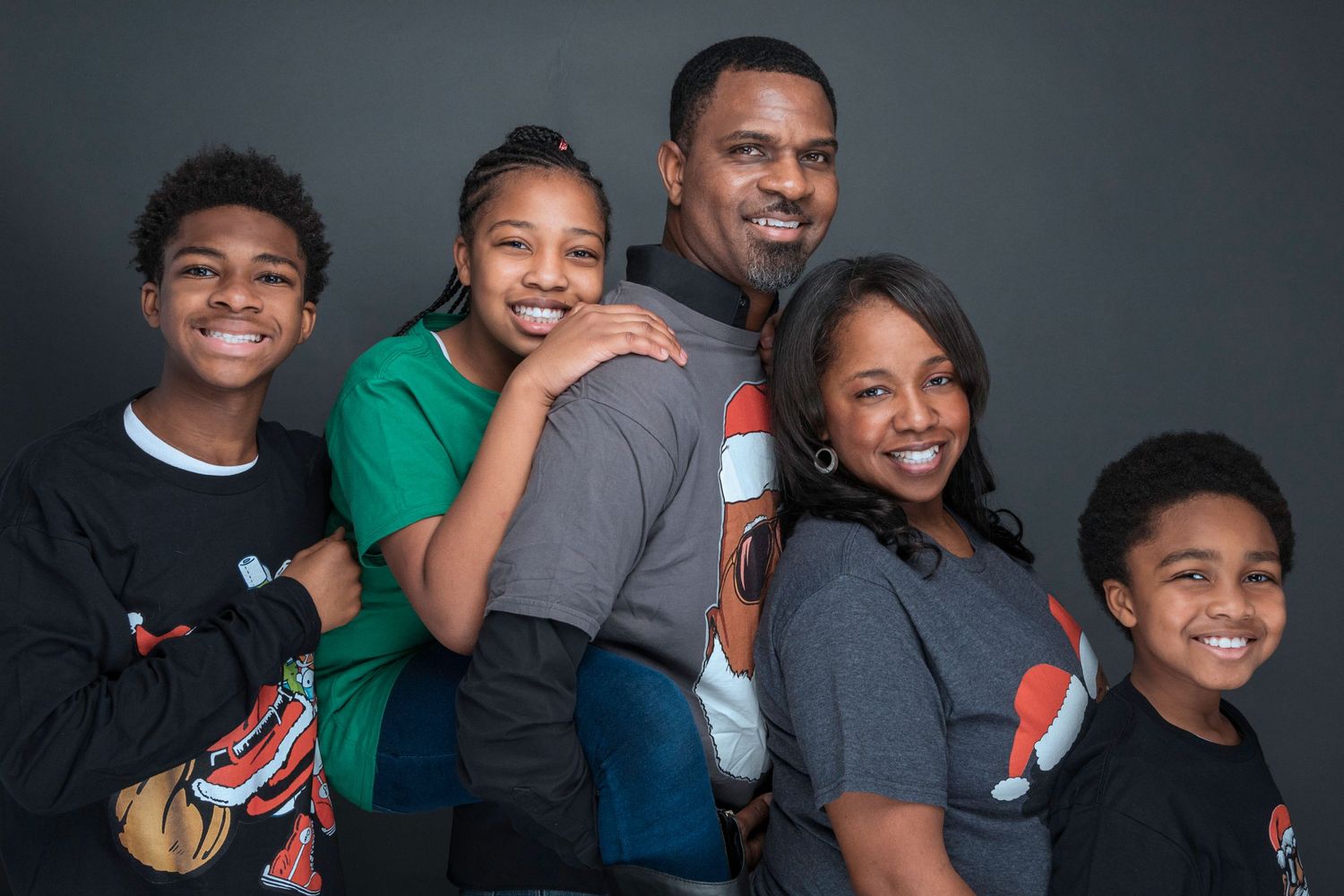A cheerful family of five poses together for a portrait against a gray background.