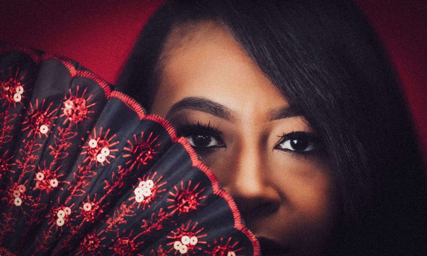 Artistic beauty portrait with decorative red fan against dark background.