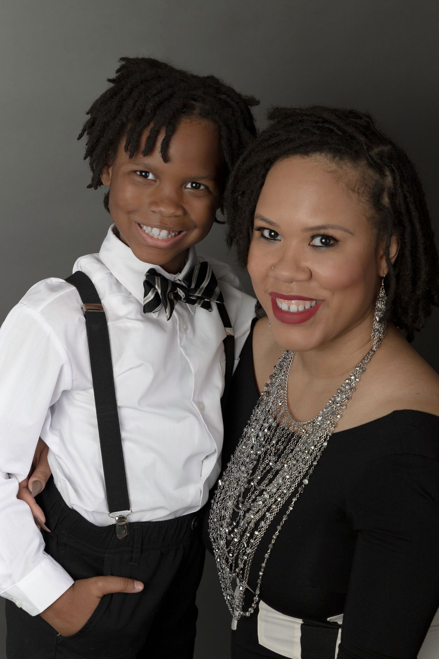 Portrait of an adult and child in coordinated formal black and white attire with suspenders and bow tie.