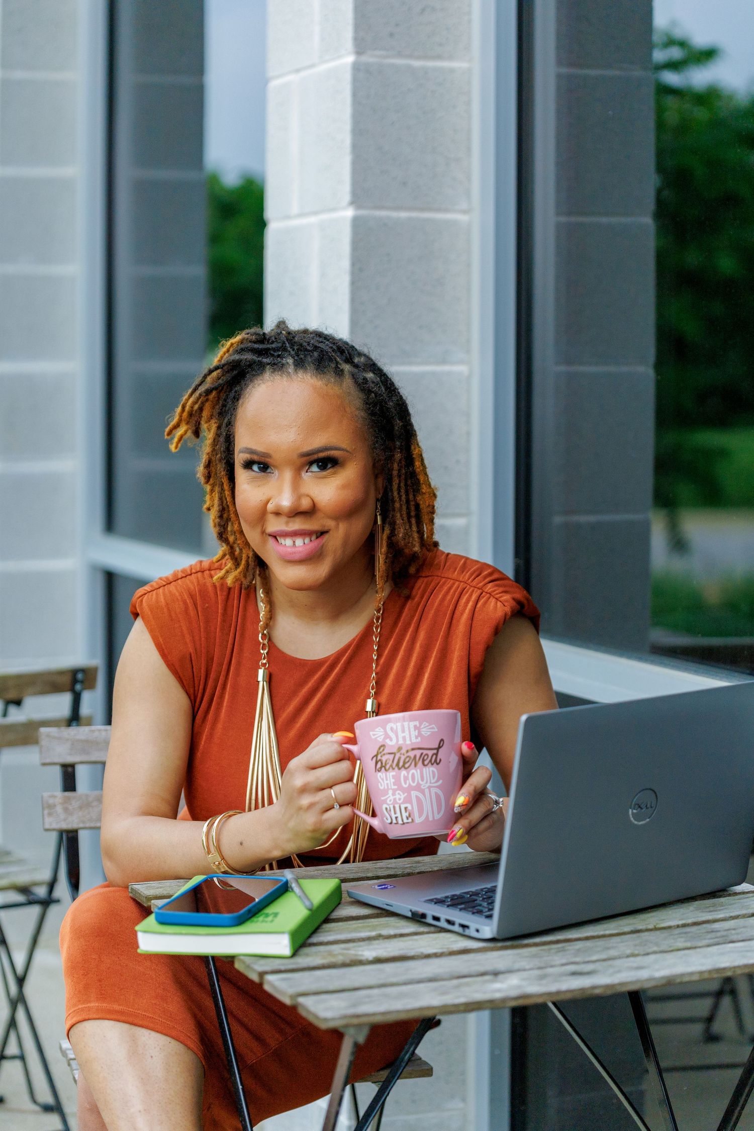 Entrepreneur working outdoors with laptop and pink mug at cafe table.