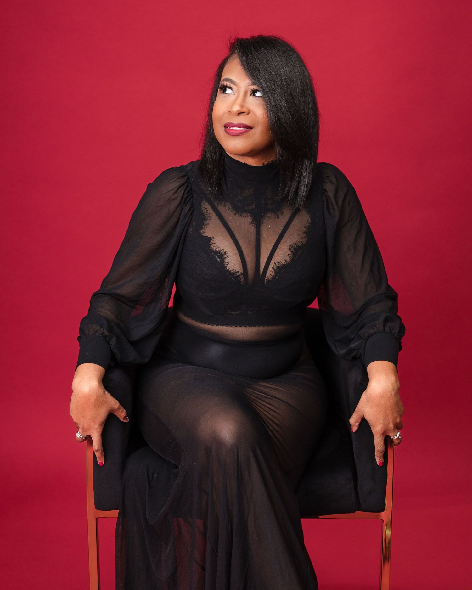 A glamour portrait against a red background featuring elegant black formal wear.