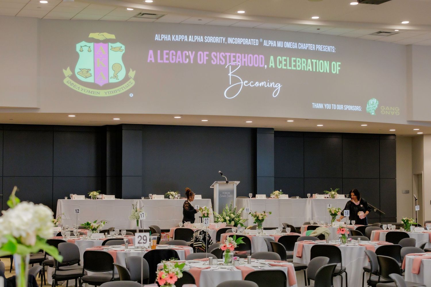 Elegant banquet hall setup with round tables decorated with floral centerpieces under event signage.