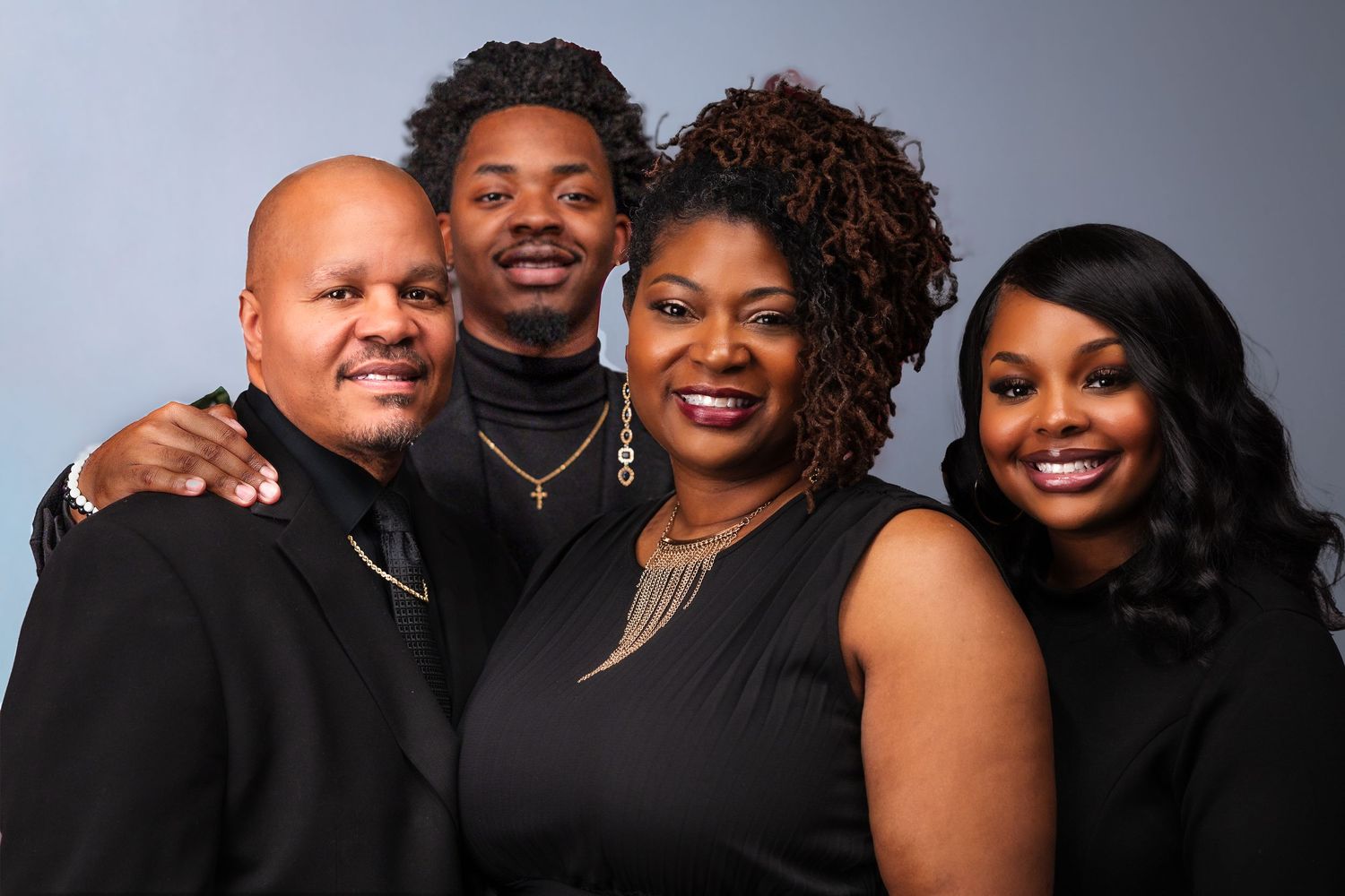 A family posed together wearing black formal attire against a gray studio background.