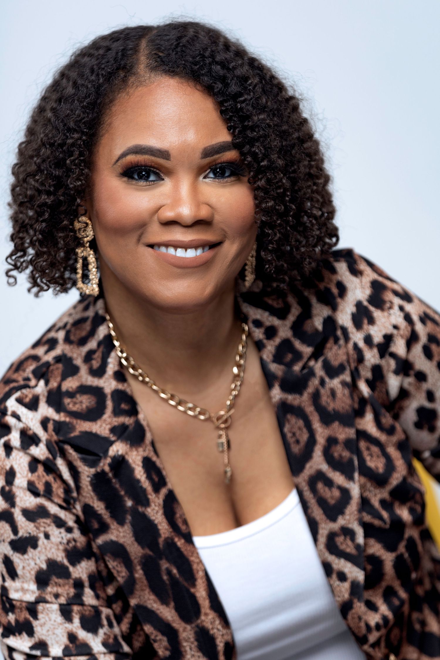 Person in leopard print and white top poses confidently with gold jewelry.
