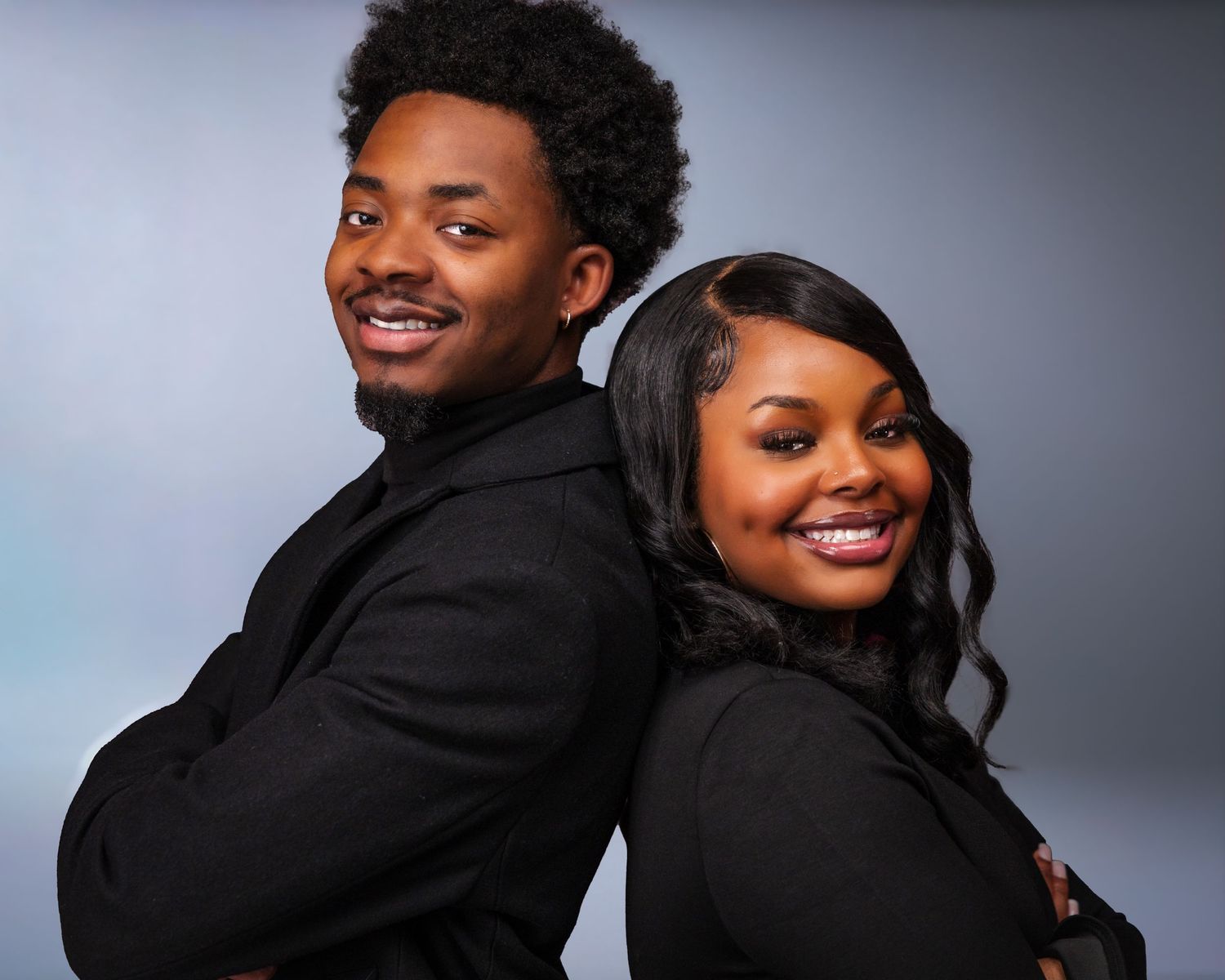 A couple in black attire poses back-to-back for a stylish studio portrait.