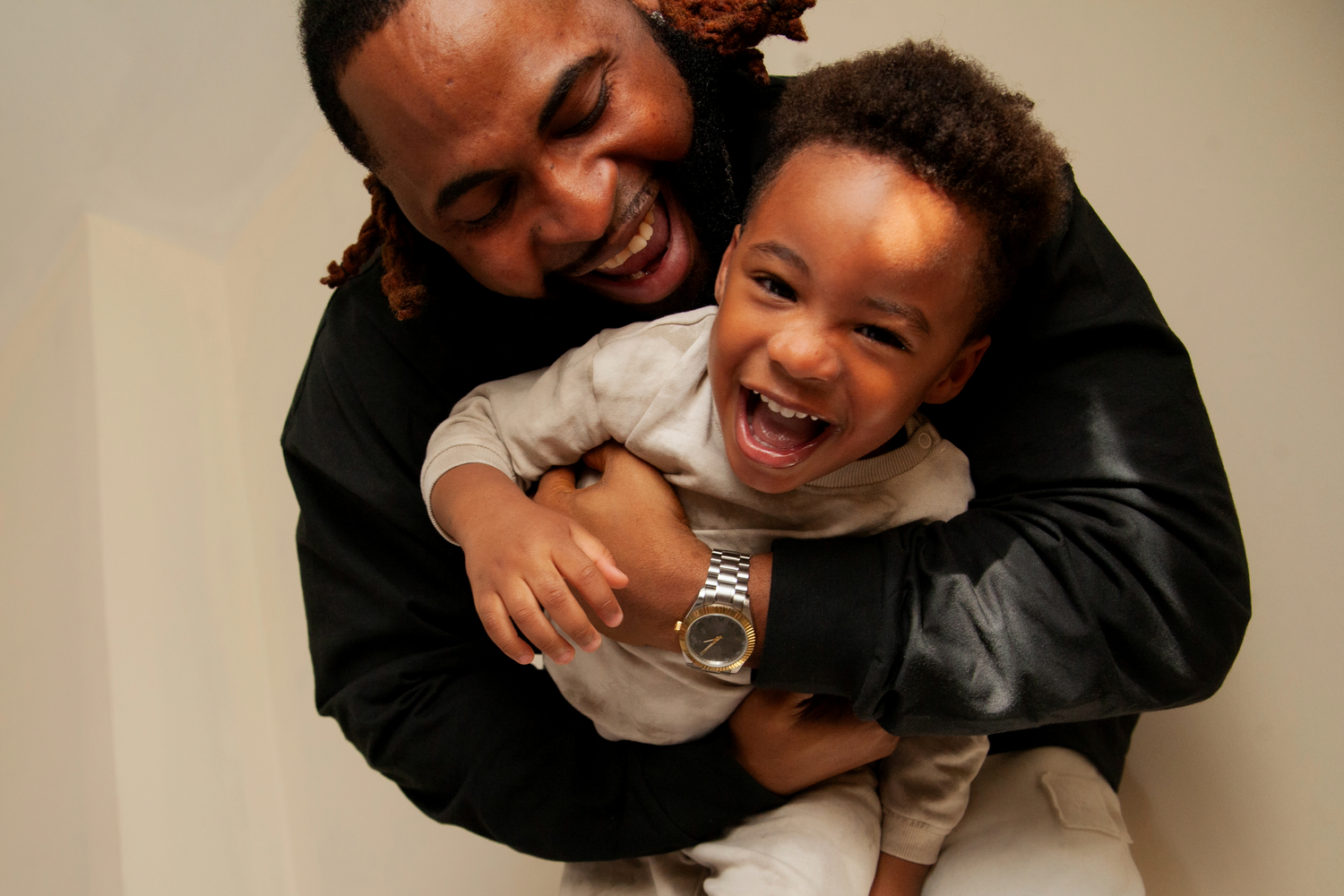 A heartwarming moment of playful embracing and laughter between parent and child against a neutral background.