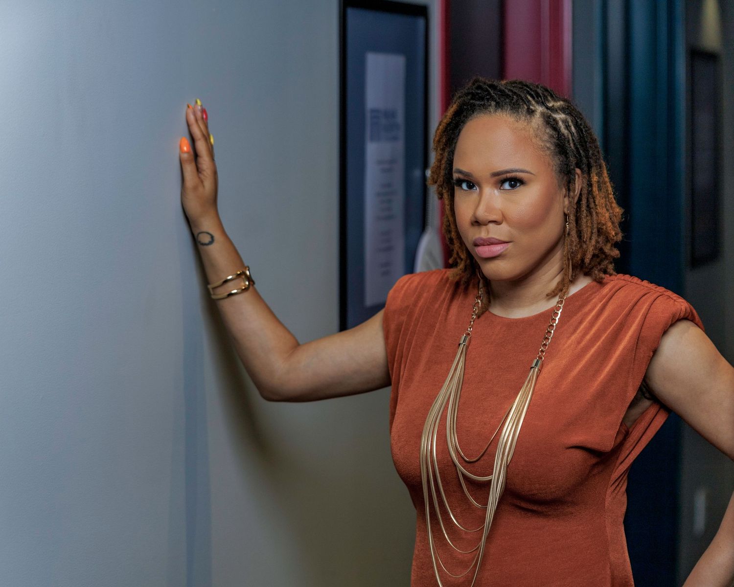 A woman in coral top with braided hair poses confidently against a dramatic background.