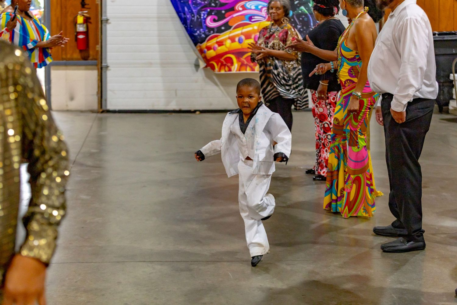 A child in a white karate uniform runs energetically across a tiled floor during an event.