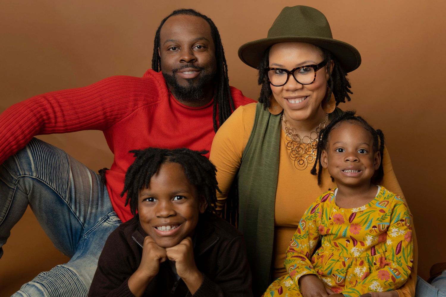 A family sits closely together wearing bright colors including red, yellow and green while posing for a portrait.