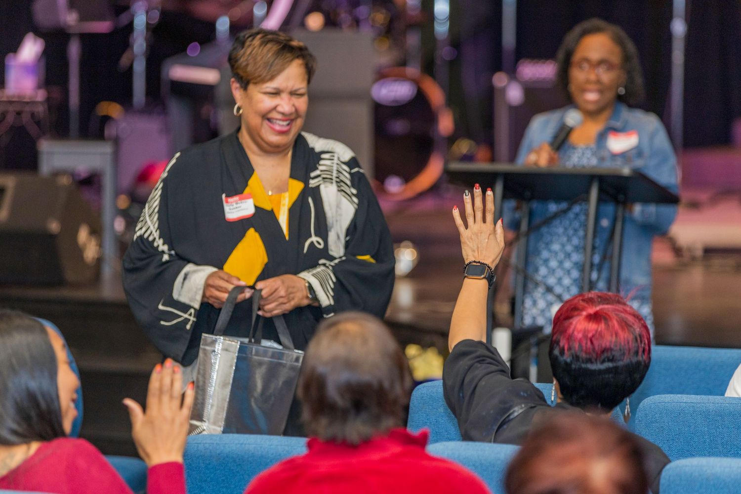 A speaker engages with an audience during a presentation event as crowd members raise their hands to participate.