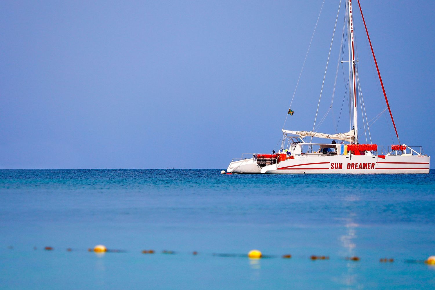 A red and white catamaran sailboat floating on calm turquoise Caribbean waters.