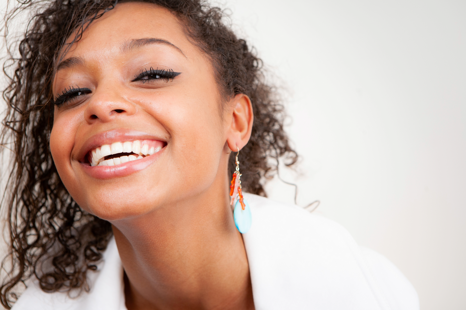 A bright smile and natural curly hair pop against a white backdrop with turquoise earrings adding a colorful accent.