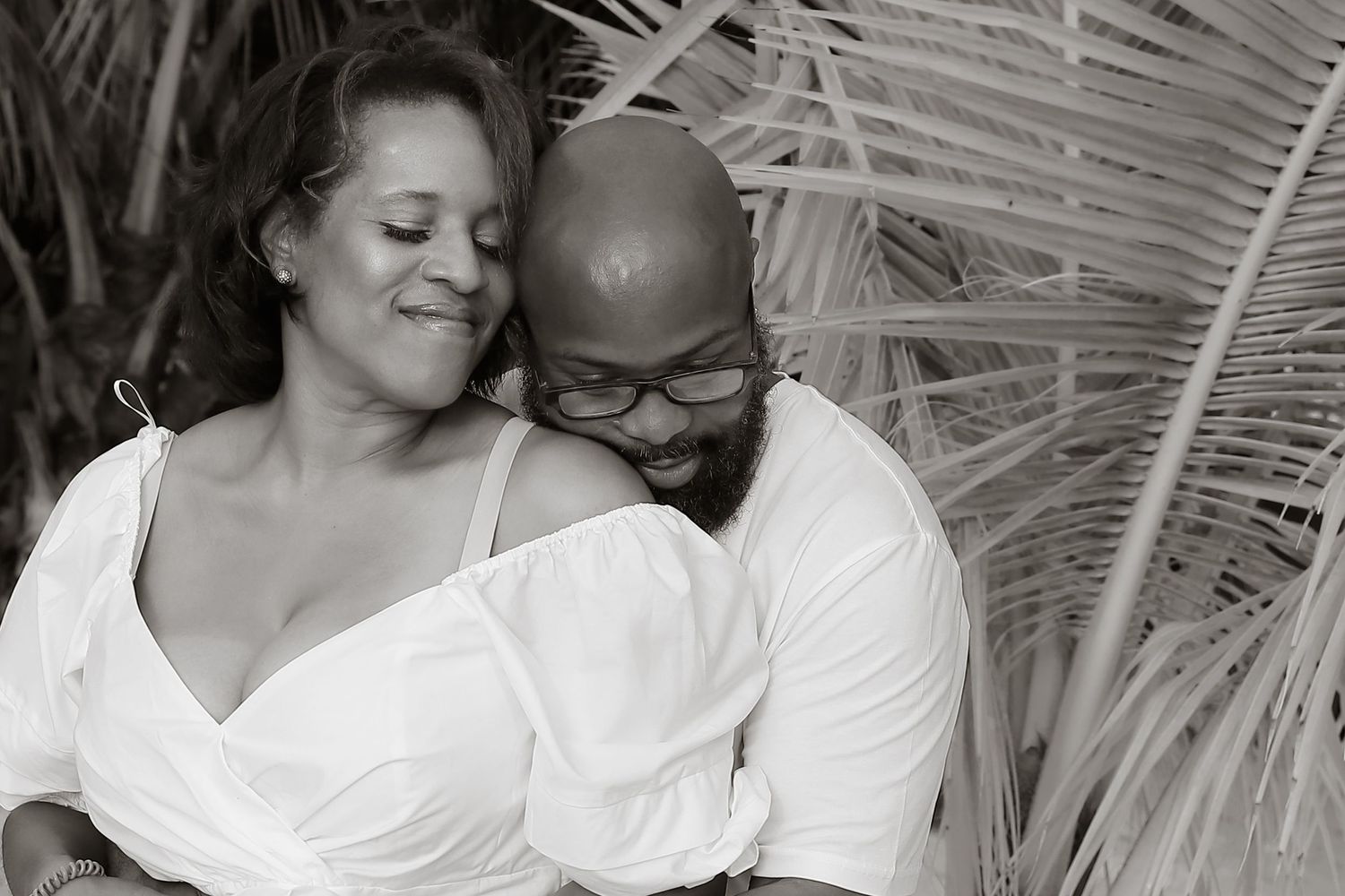 A romantic black and white portrait of a couple sharing an intimate moment among tropical palm fronds.