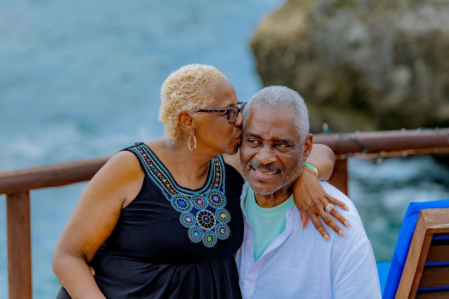 Loving couple embraces on outdoor deck with ocean view while sharing intimate moment together.