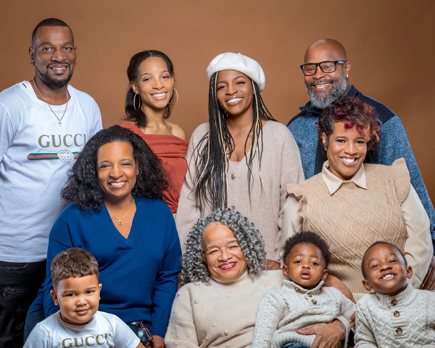 A multi-generational family poses together for a formal portrait against a brown background.