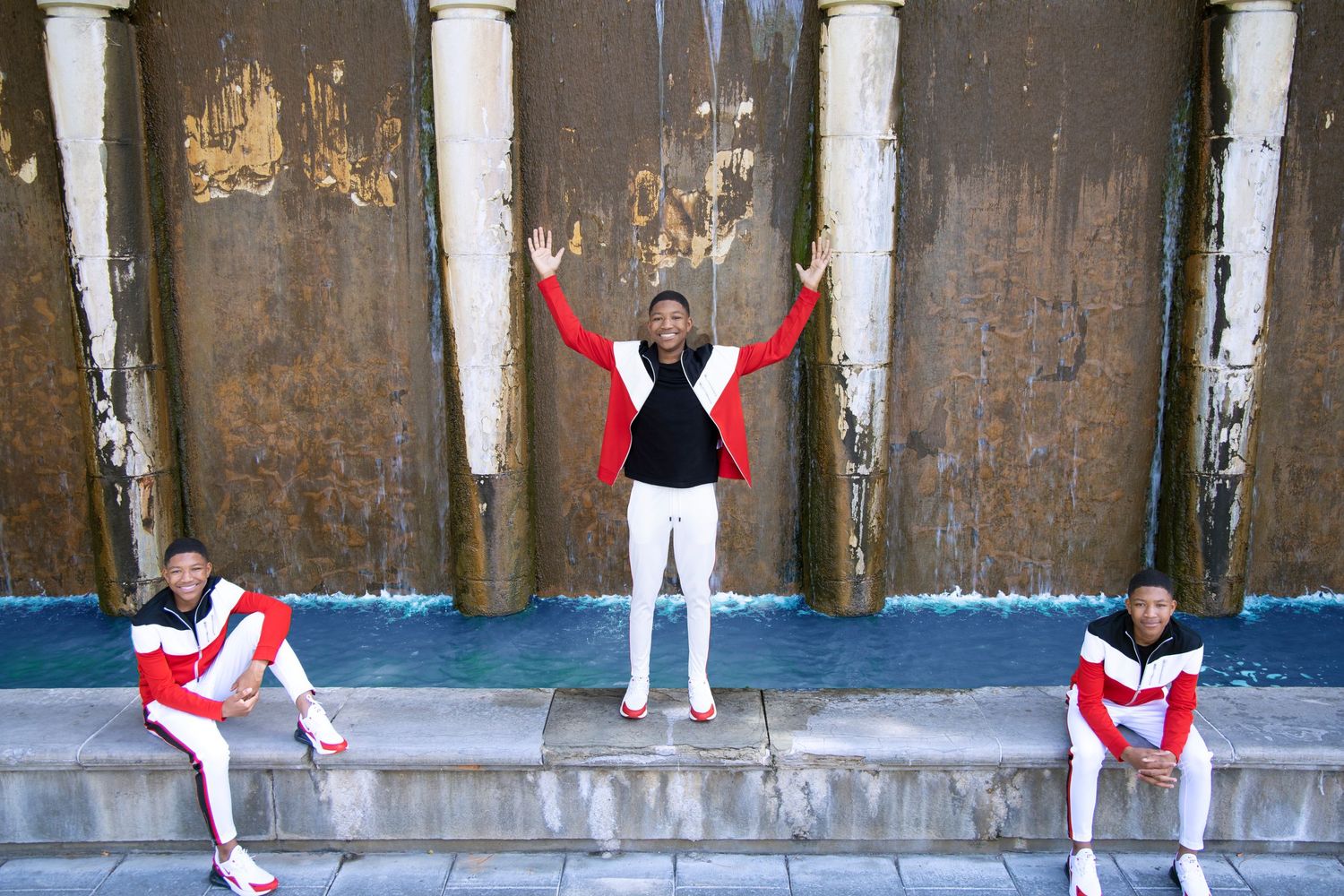 Young man in red and white outfit pose dramatically three different ways on a concrete ledge.