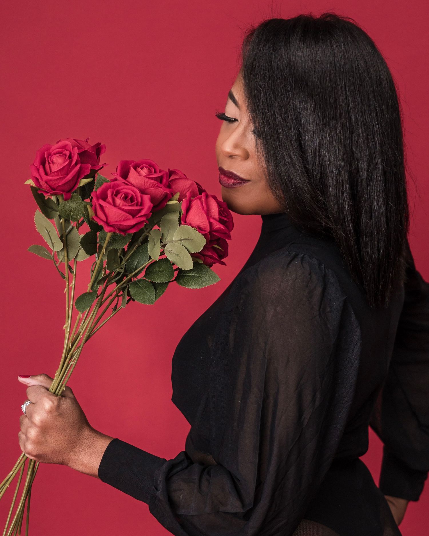 Artistic portrait featuring roses being held against a vibrant red background.