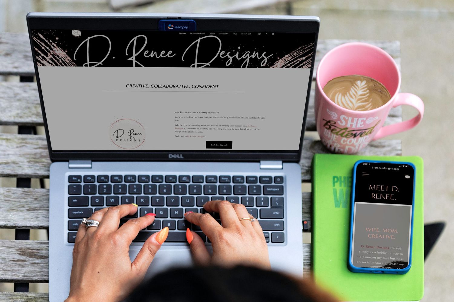 Hands typing on laptop with pink coffee mug and phone on wooden desk.