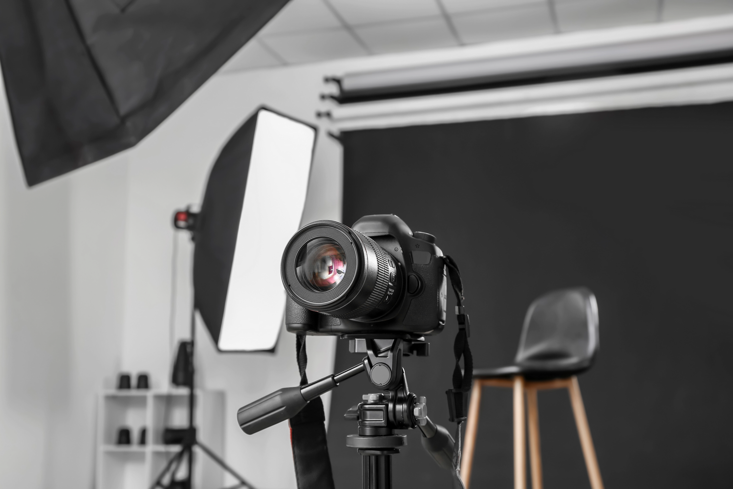 Professional photography studio setup with DSLR camera on tripod and softbox lighting equipment against white wall.