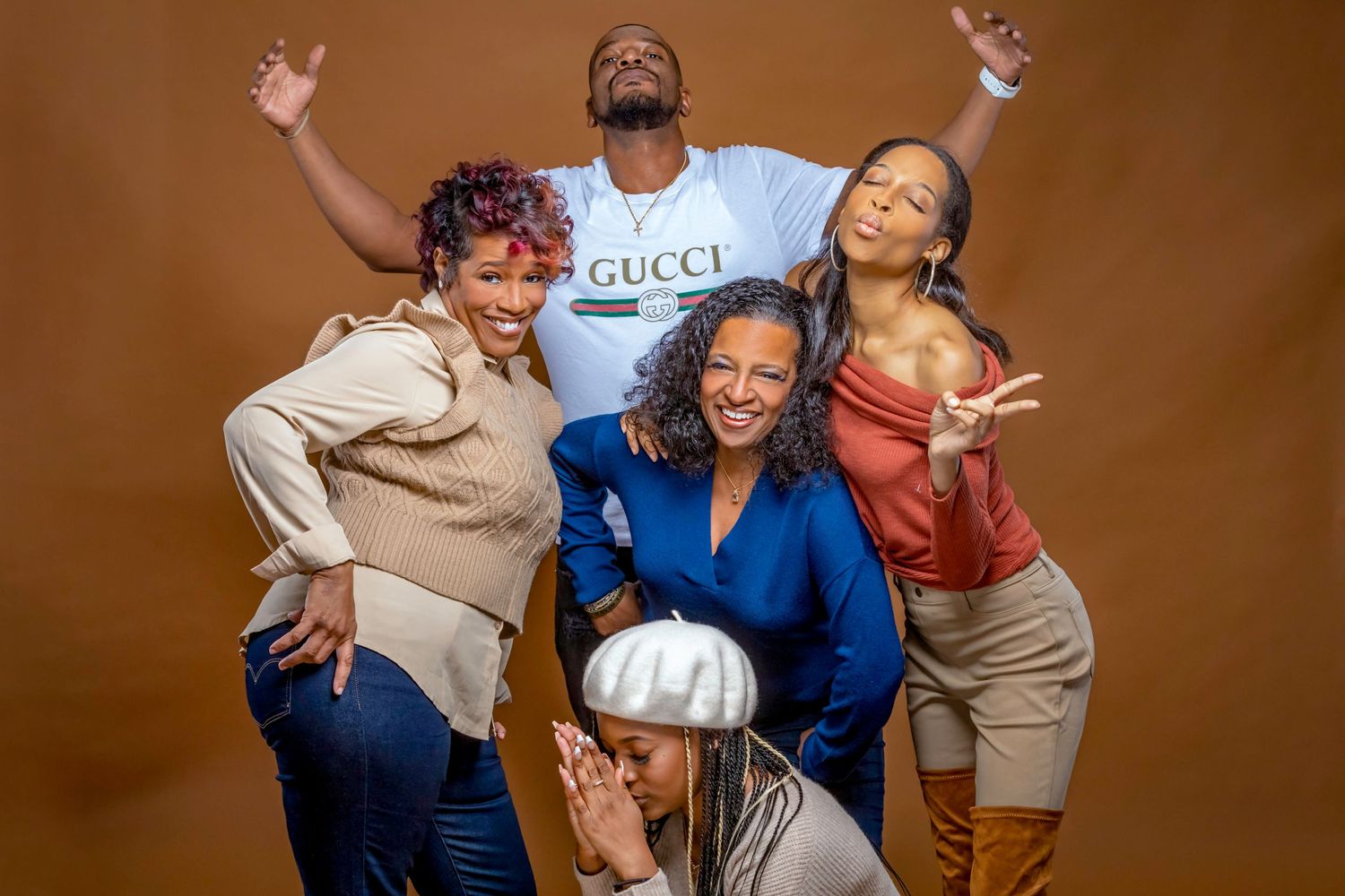 A group poses playfully together in casual attire against a brown studio backdrop.