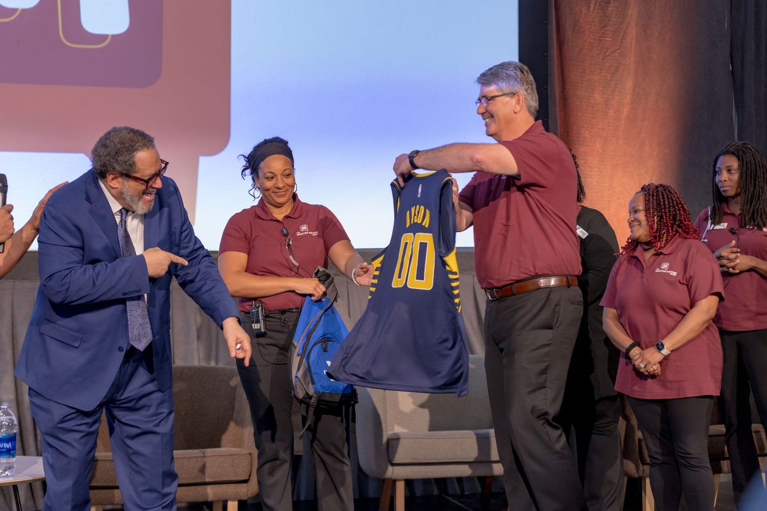 Event participants examine contents of a blue bag during an on-stage presentation.