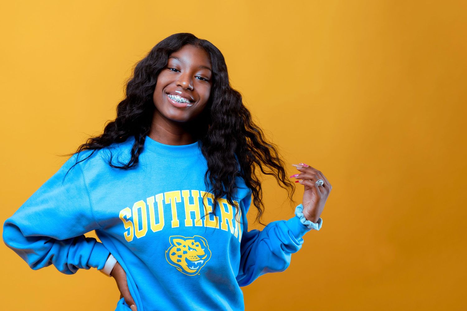 Young woman in blue Southern sweatshirt poses playfully against yellow background.