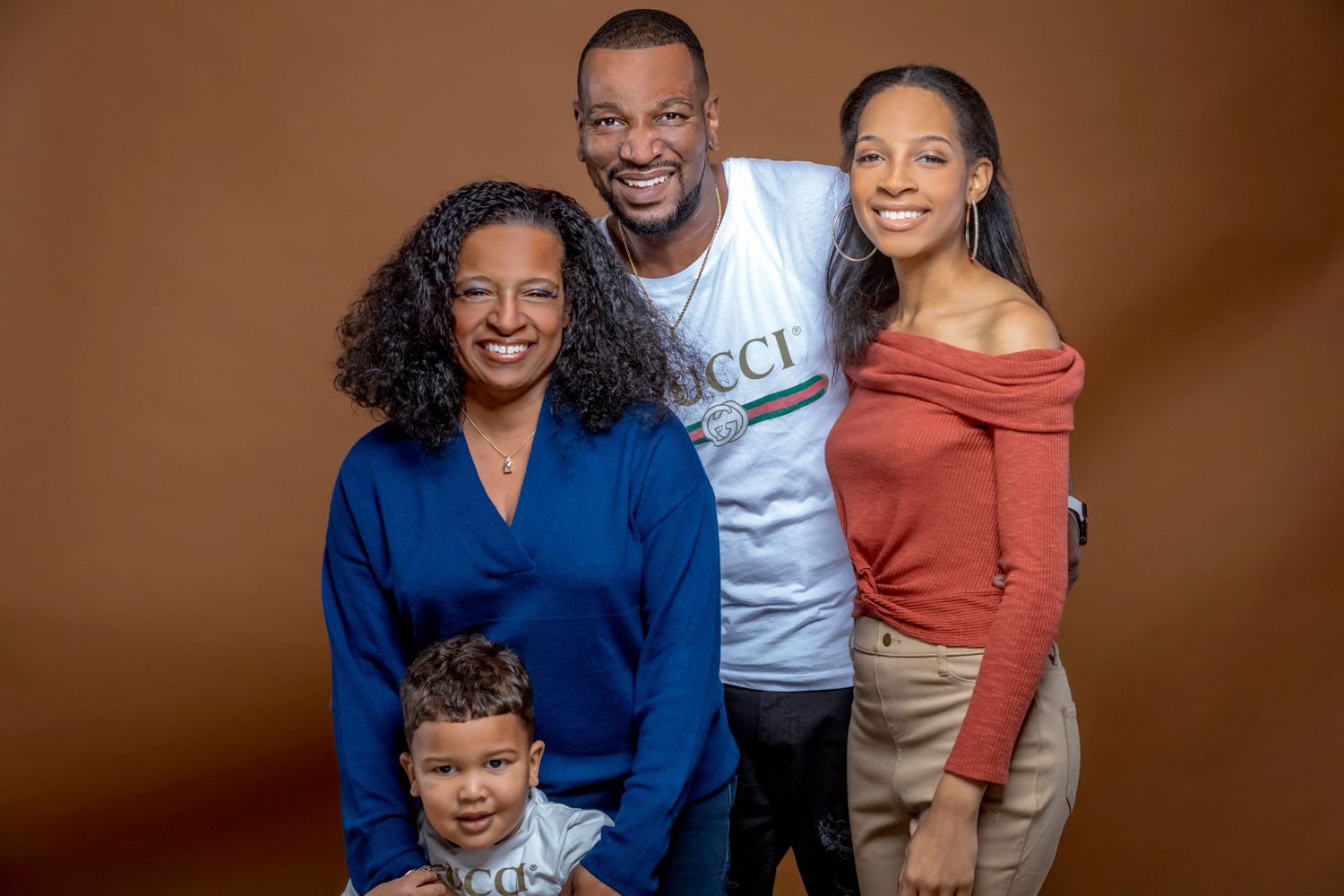 Family portrait featuring coordinated casual outfits against brown background.