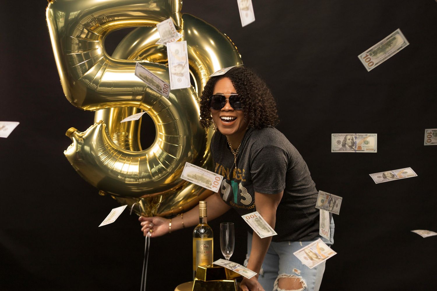Festive birthday celebration with gold number 50 balloons and falling money against black background.