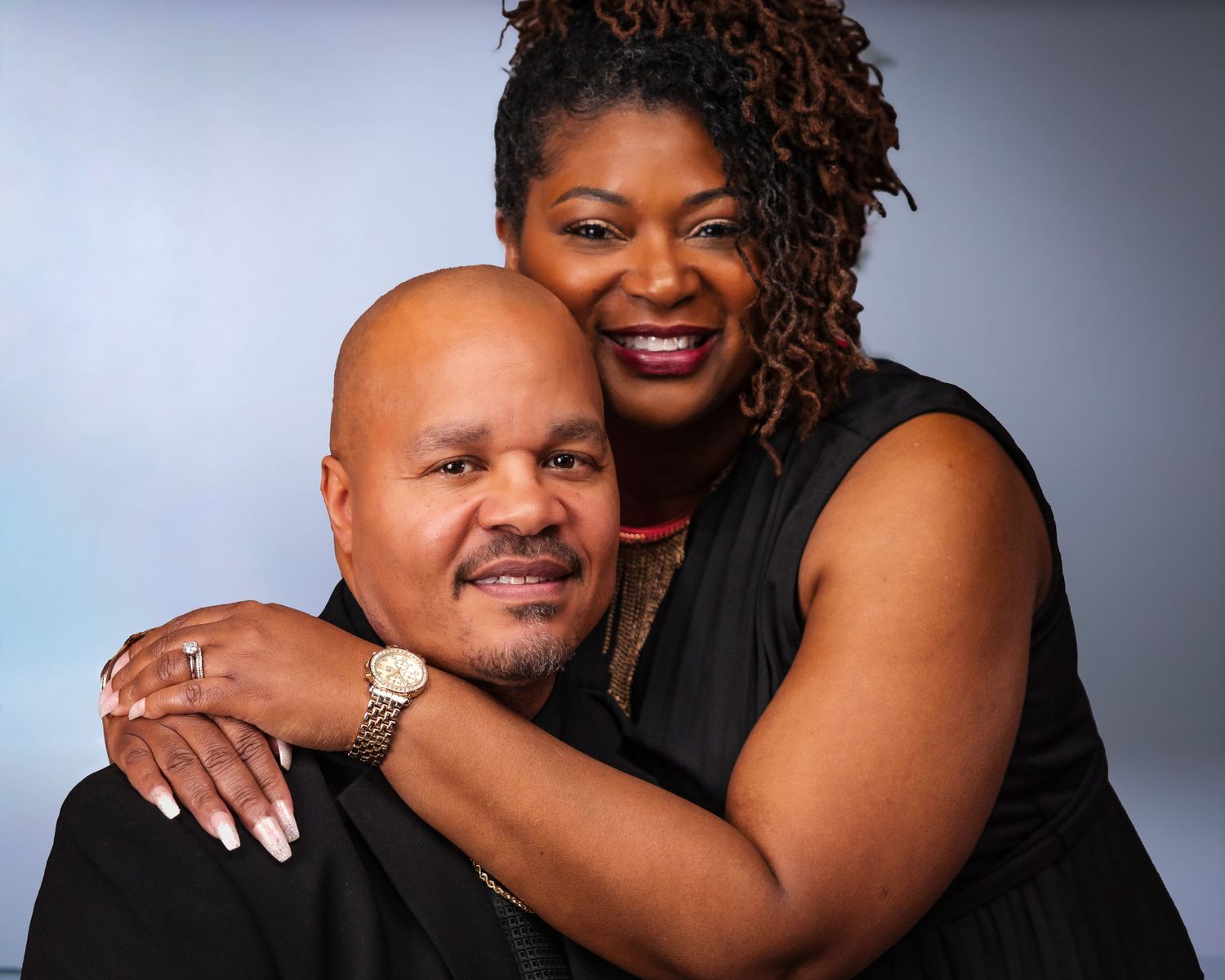 Elegant couple in formal black attire embracing in studio portrait.