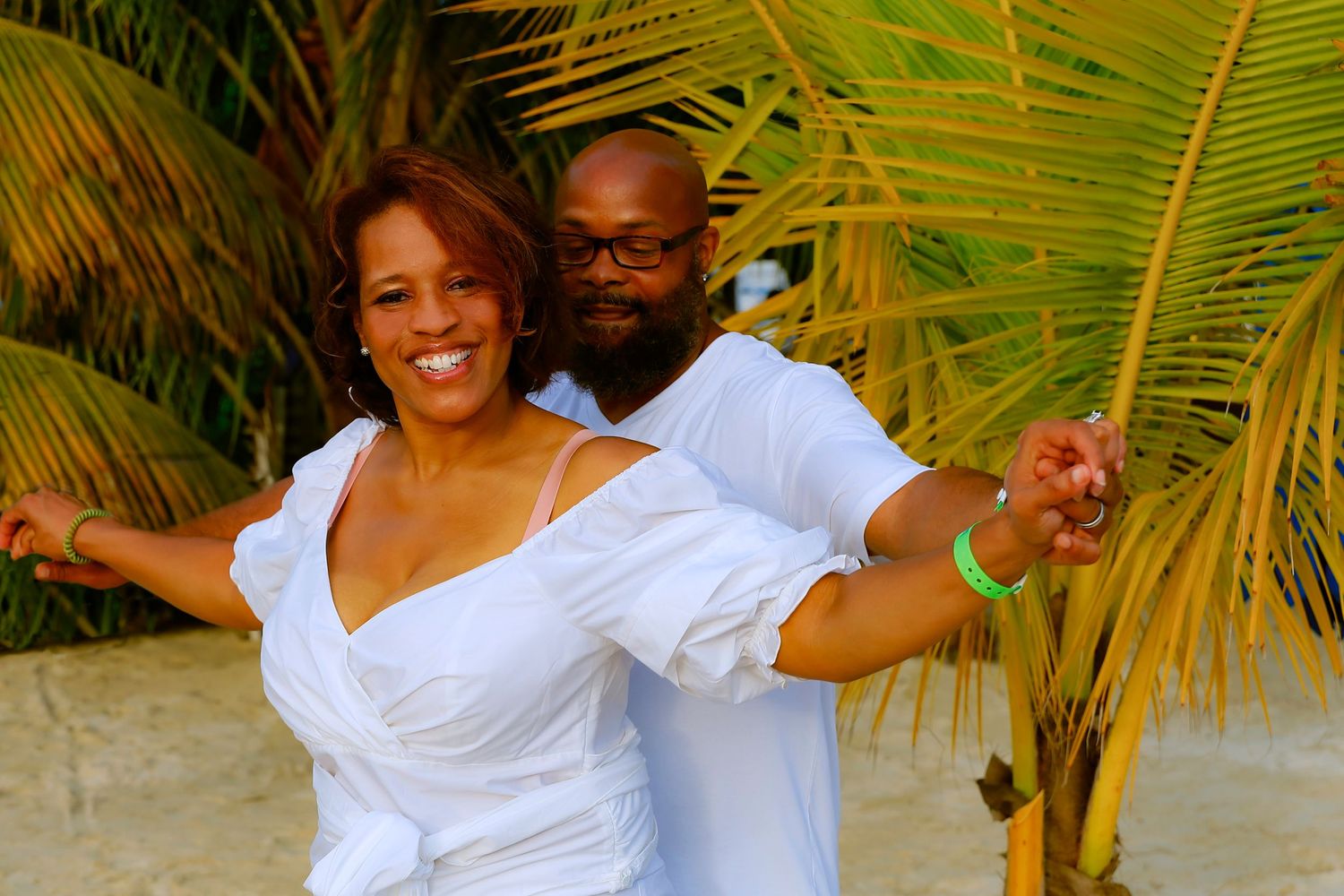 Joyful couple dancing together among palm trees on tropical beach.