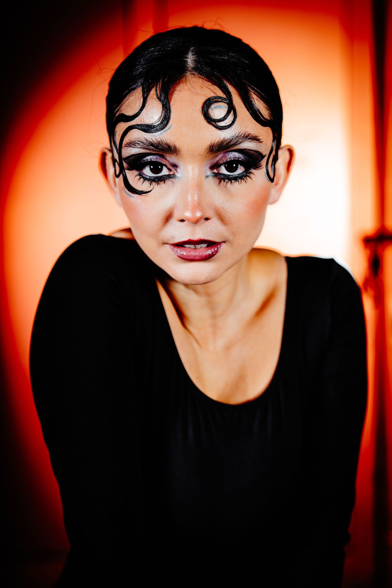 a performer staring into the camera, with red in the background, a close up