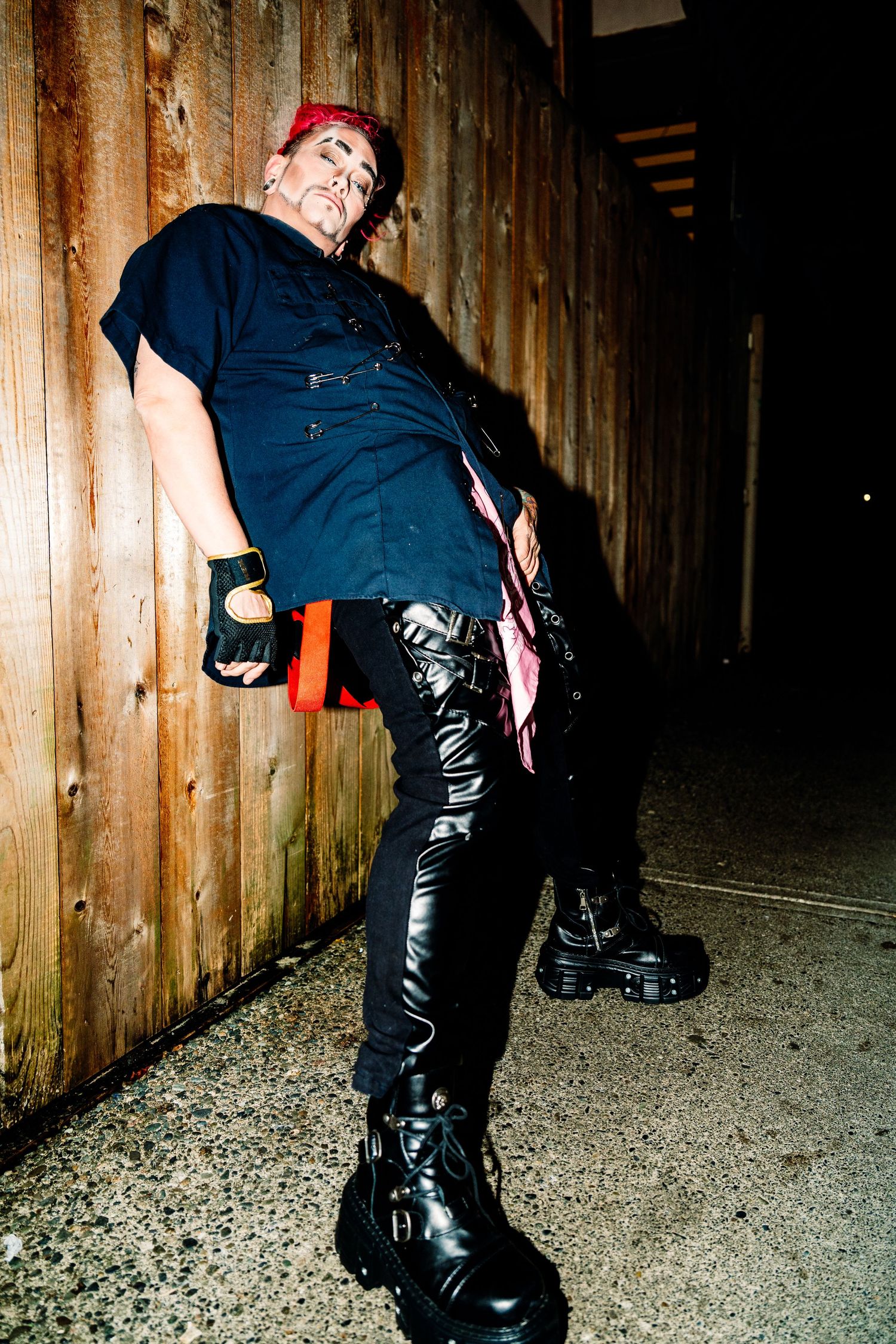 drag performer posing, leaning against the wall looking at the camera