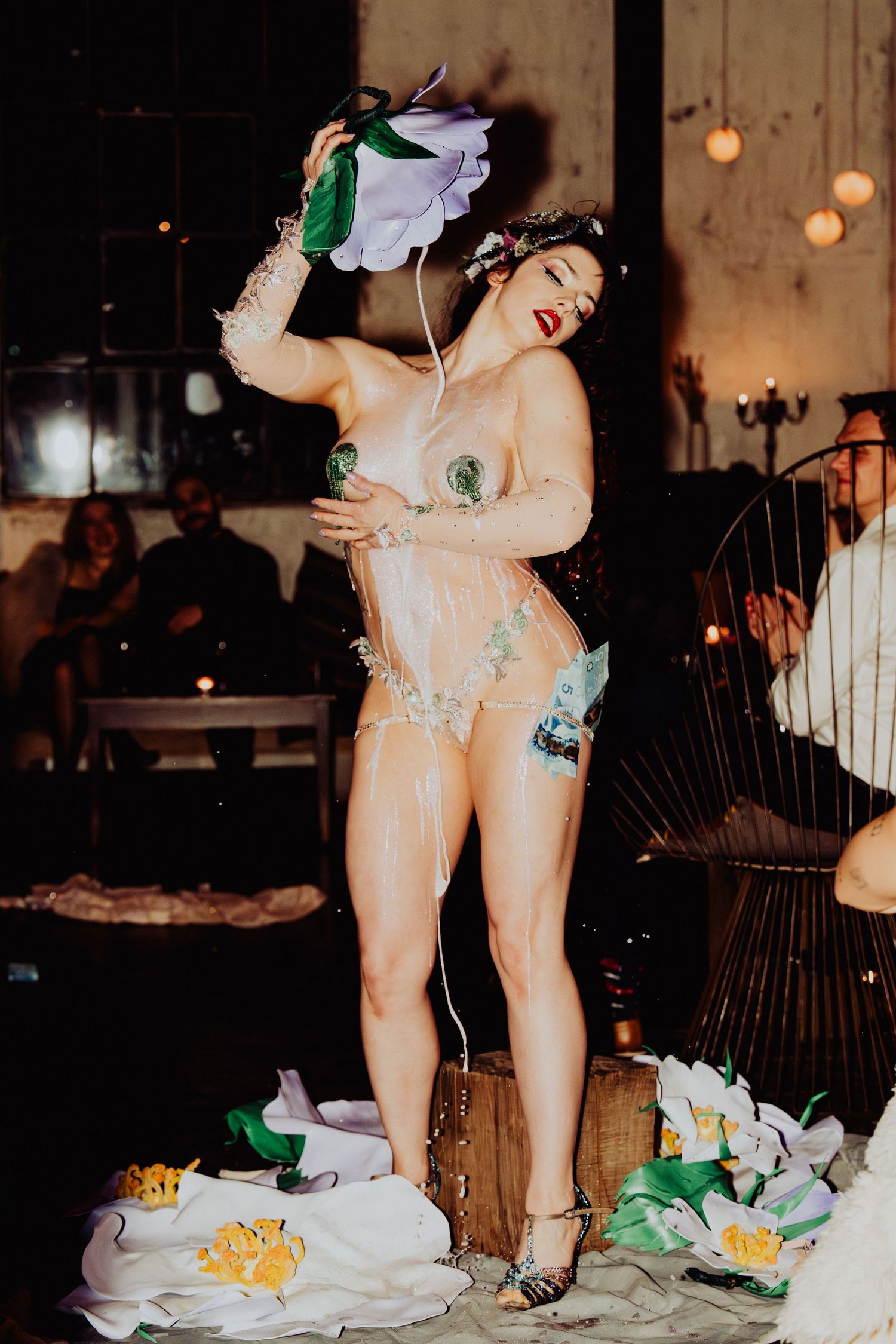 performer shot on floor stage, pouring a milk texture on the body