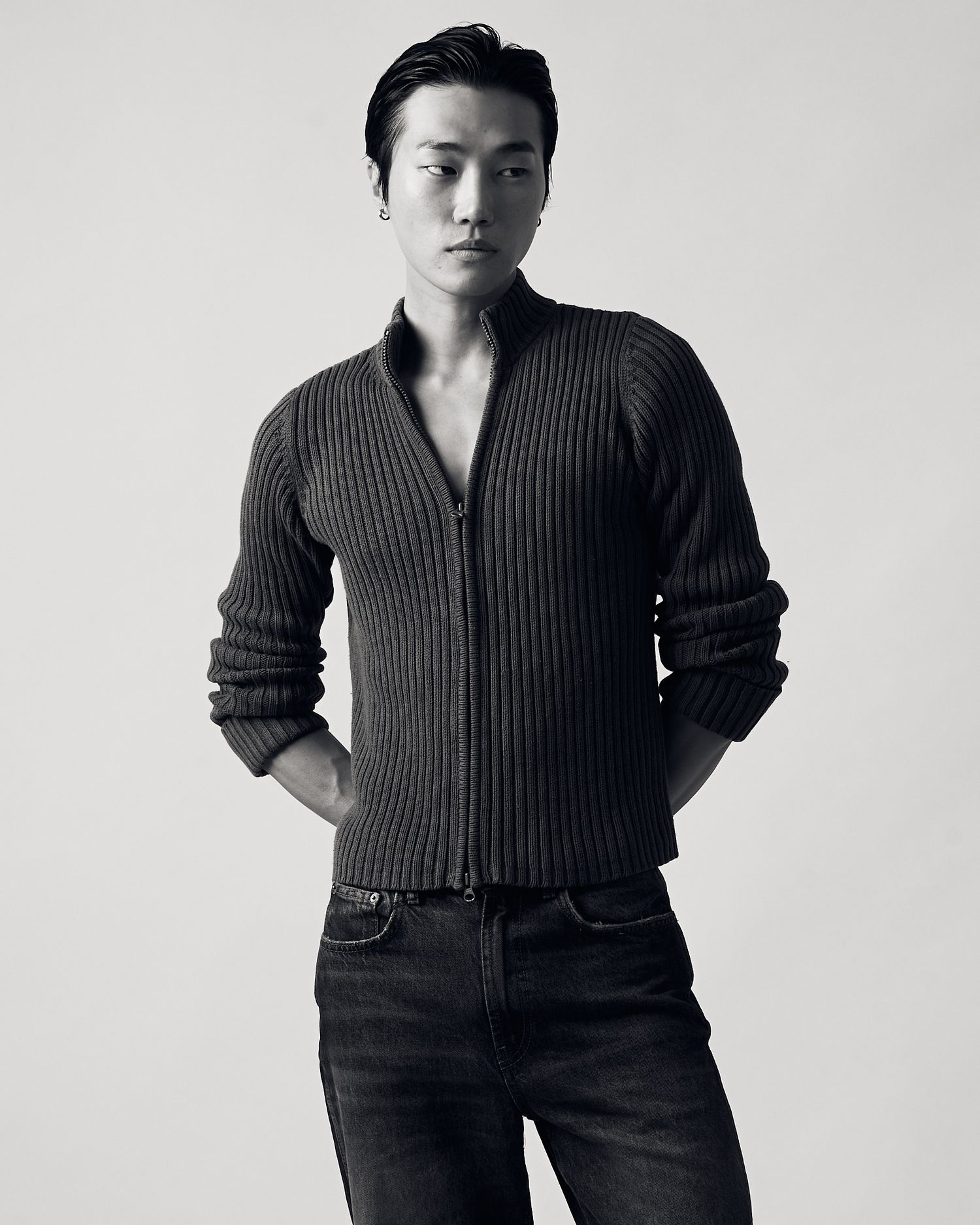 A person poses in a black ribbed sweater and dark pants in a series of three black and white fashion photographs.